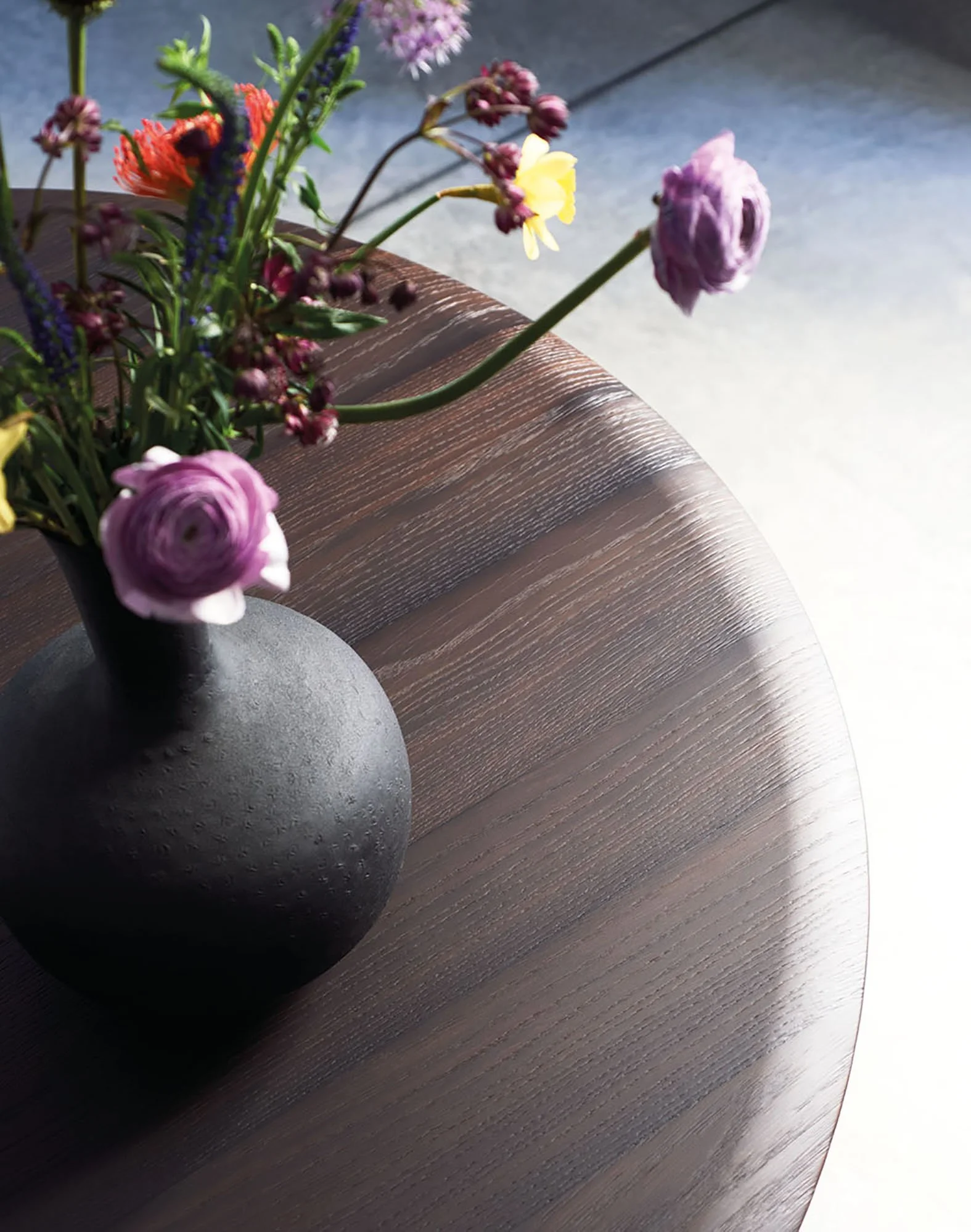 Blumen in einer schwarzen Vase auf einem Holztisch, Sonnenlicht fällt auf die Oberfläche.