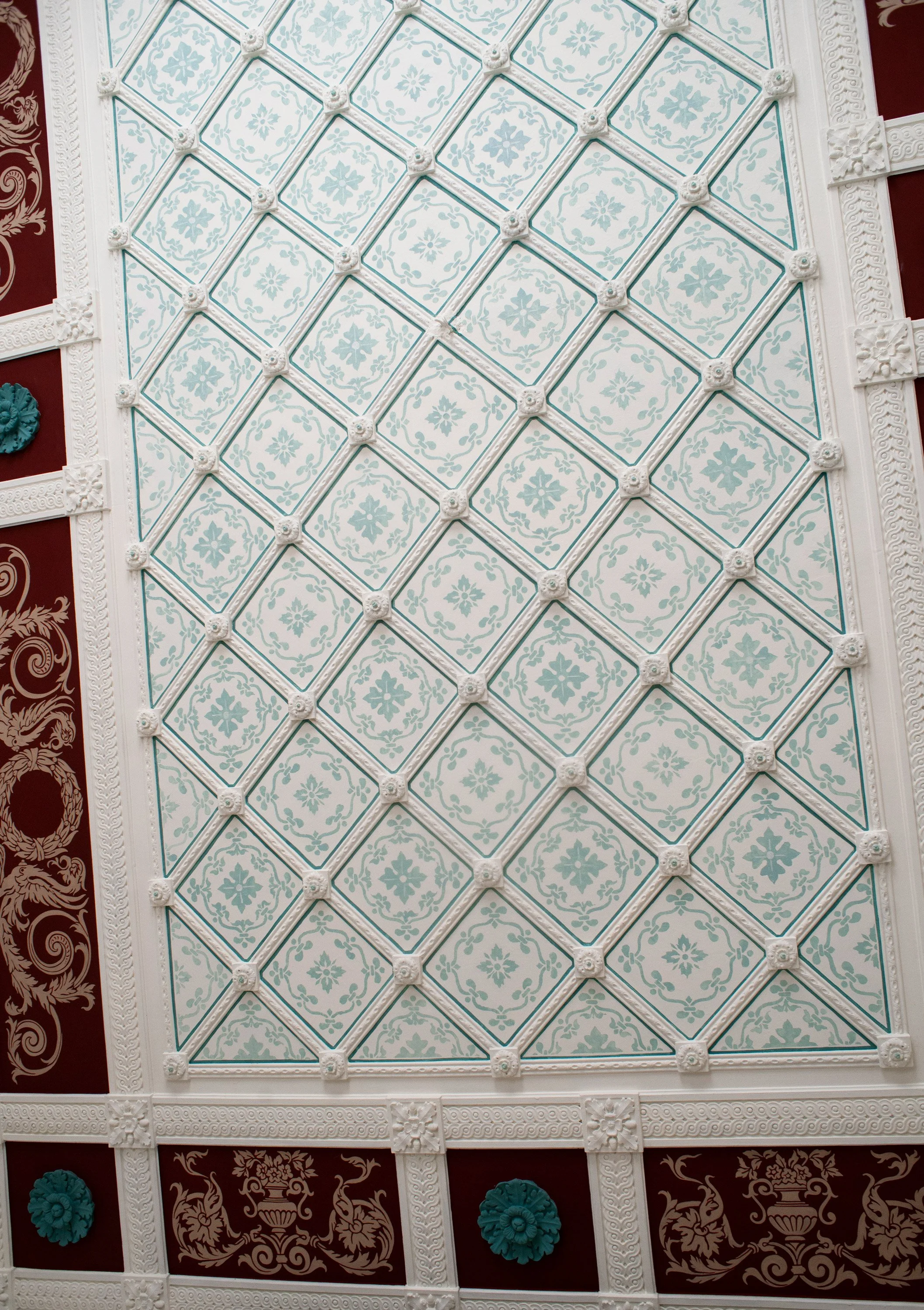 Dekorativer Deckenbereich mit weißen und blauen Mustern, Verzierungen und stilisierten Elementen, umgeben von dunklen Wänden mit goldenen Ornamenten und blühenden Motiven.