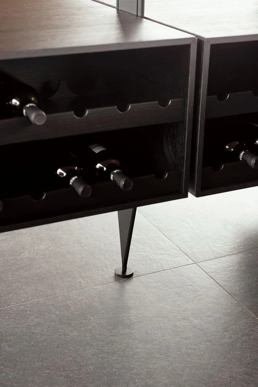 Weinregal mit mehreren Flaschen Wein, Möbel aus dunklem Holz, metallene Tischbein, moderne Raumgestaltung.