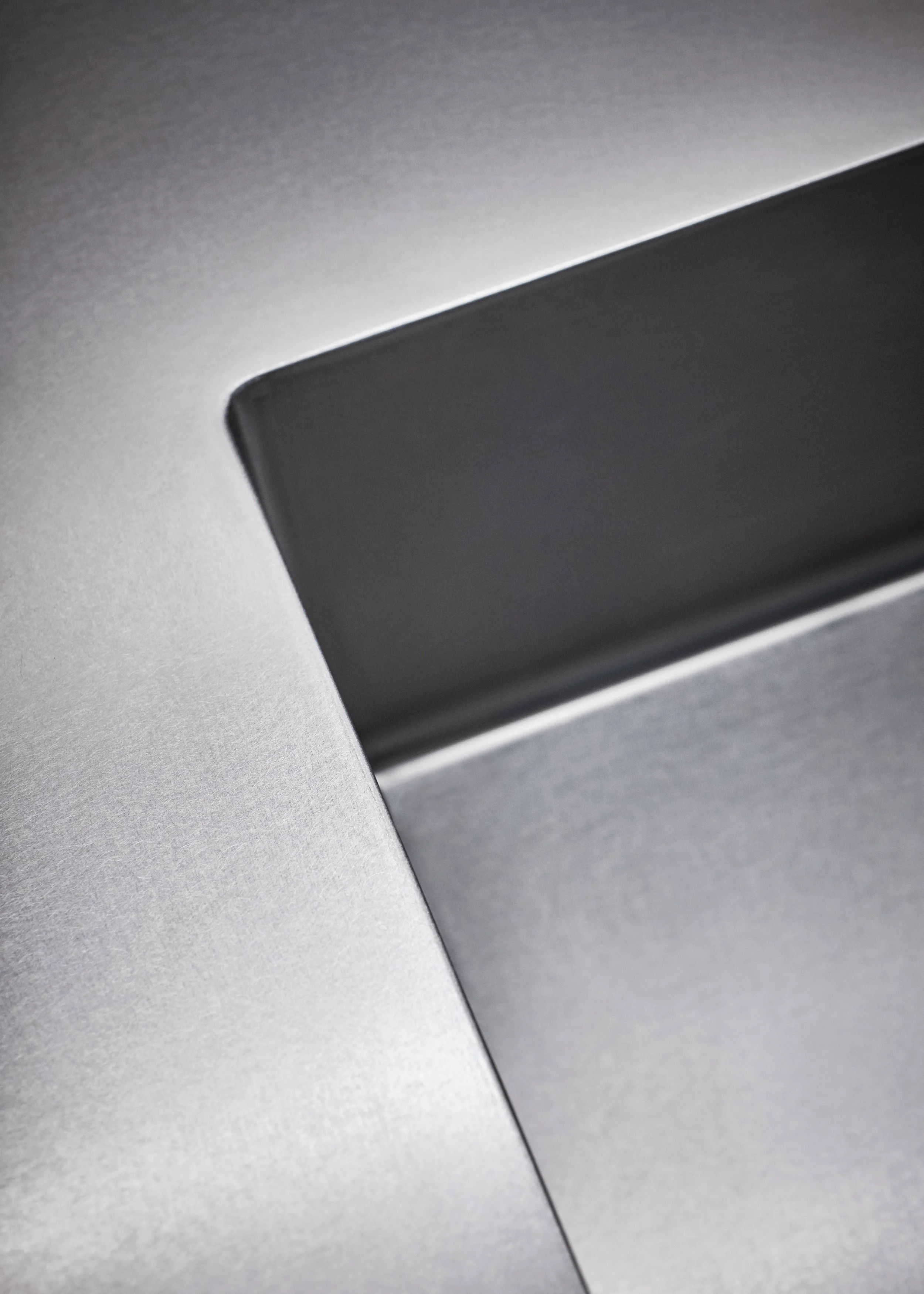 Nahaufnahme des Ecke eines Laptops, Fokus auf das argentumfarbene Metallgehäuse und einen schwarzen Bereich, möglicherweise ein Touchpad oder Bildschirmrand.