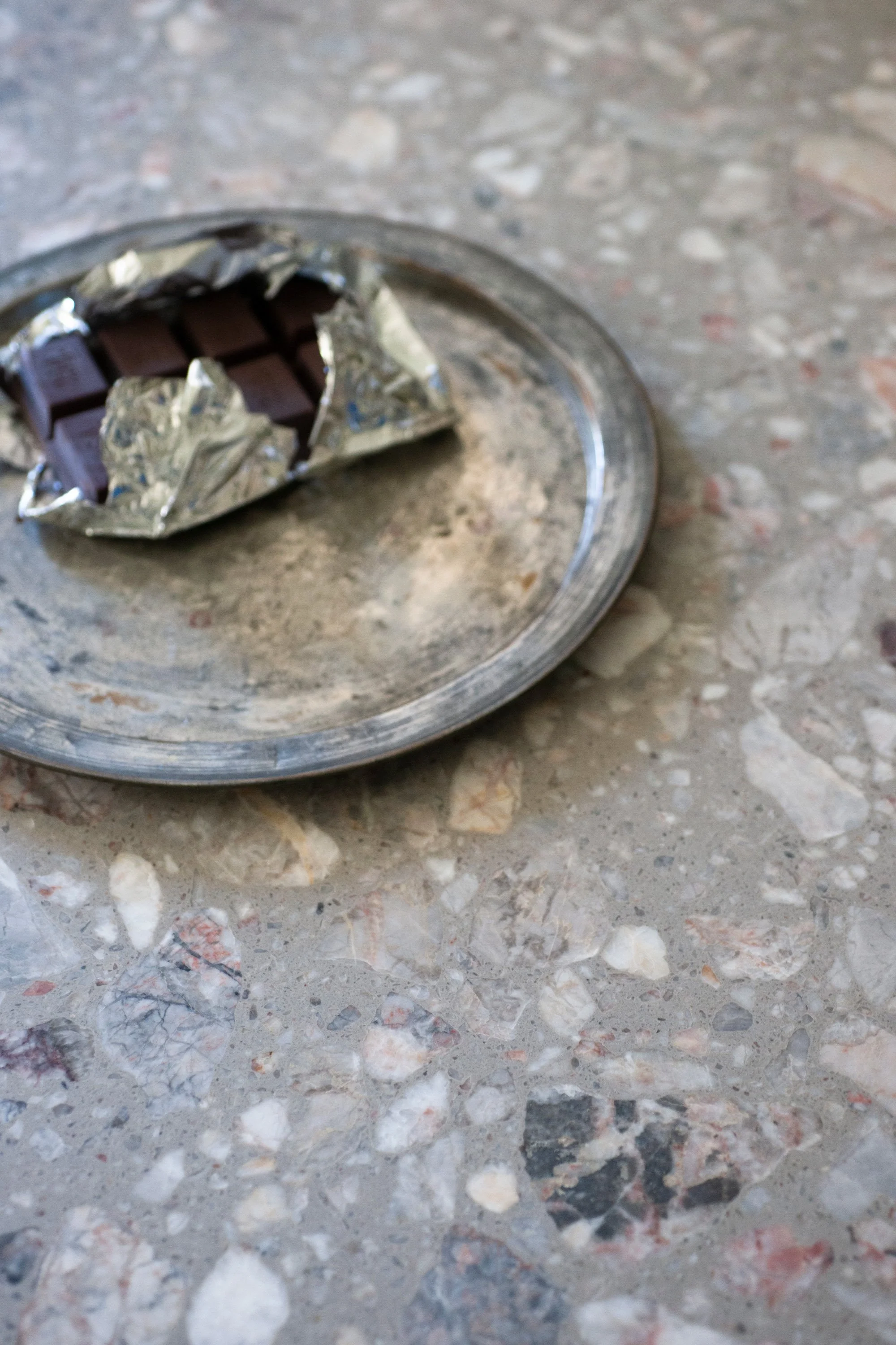 Eine zerbrochene Schokoladentafel in Aluminiumfolie auf einem Marmor- oder Steinboden.