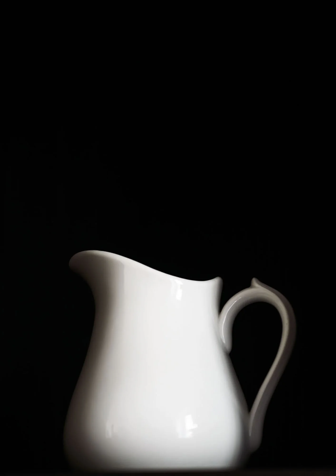Ein weißer Kaffeekrug mit geschwungener Form vor schwarzem Hintergrund.