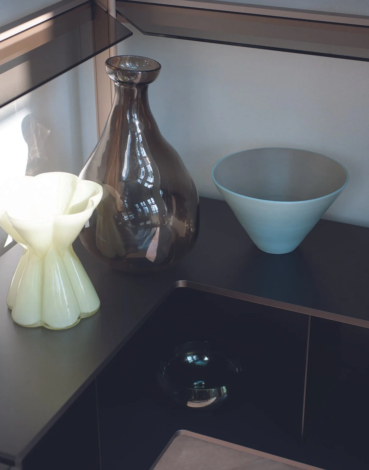 Drei dekorative Gefäße auf einer schwarzen Theke, darunter ein schwarzer Glasvase, eine weiße Blumentopf und eine großen blauen Schüssel.