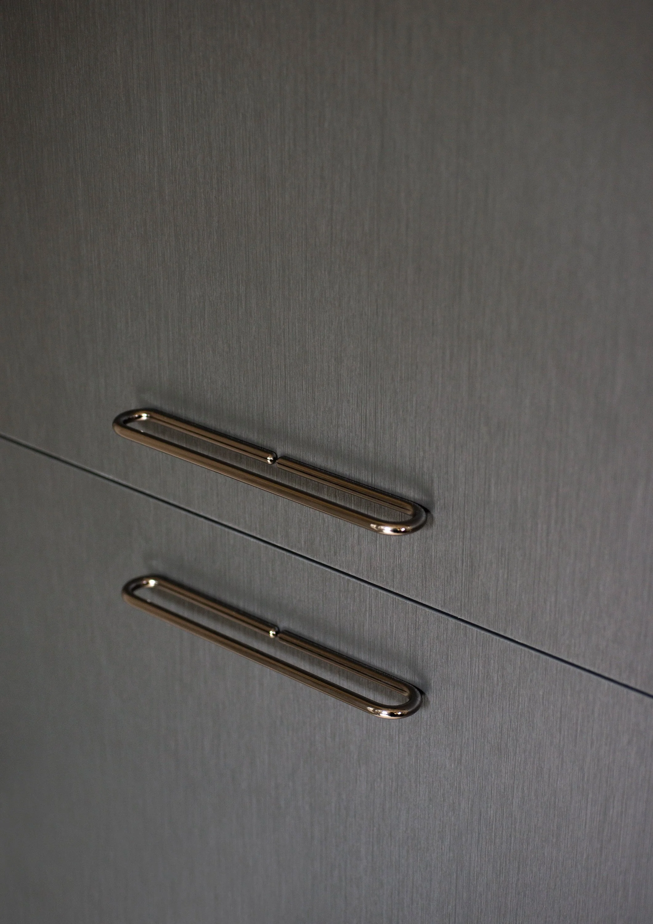 Nahaufnahme eines grauen Schranks mit drei horizontalen Griffen aus Metall.