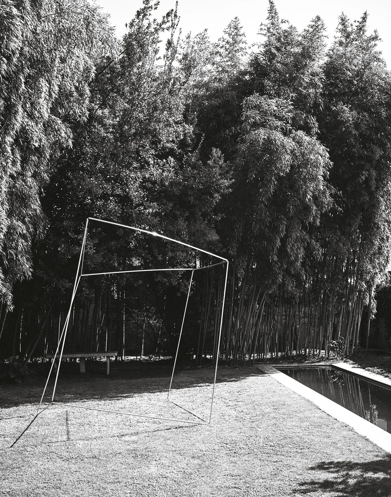 Ein Garten mit Bäumen und einer Orangerie im Hintergrund. Im Vordergrund ist ein Spielgerüst aus Metall in Form eines Würfels, eine Bank und ein Kinderkarussell.