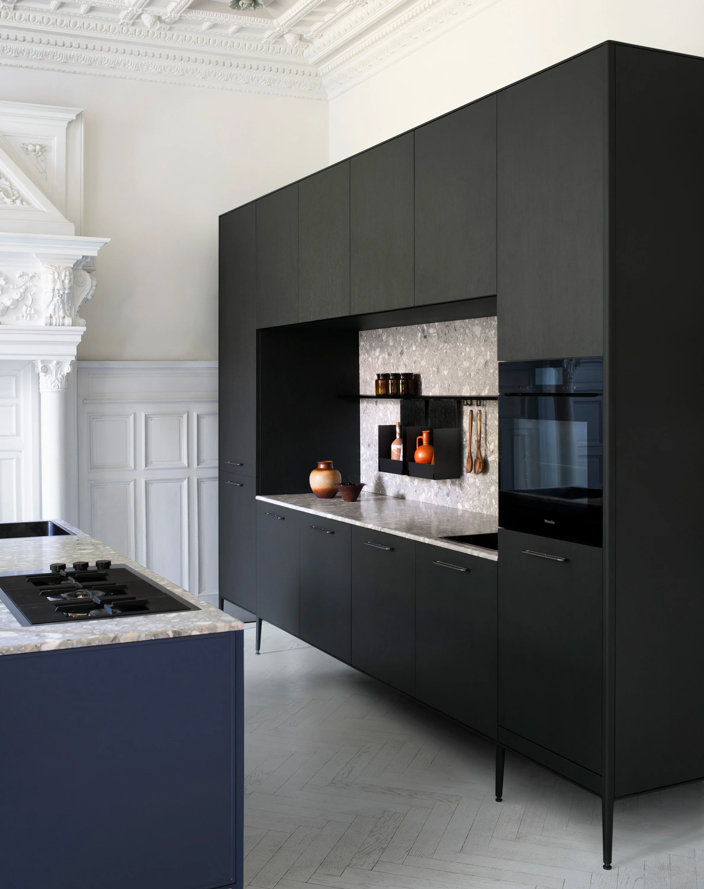 Moderne schwarze Küchenschrankwand mit Marmorküche und dekorativen Vasen und Kochutensilien in einer eleganten, historischen Raumgestaltung.