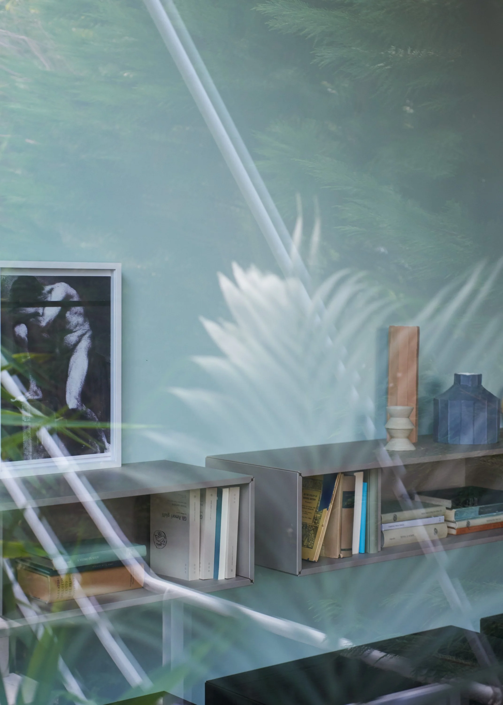 Ein Bücherregal mit Büchern, einem gerahmten Pandabild, einer Vase und einem blauen Hausmodell, gesehen durch eine Fensterscheibe