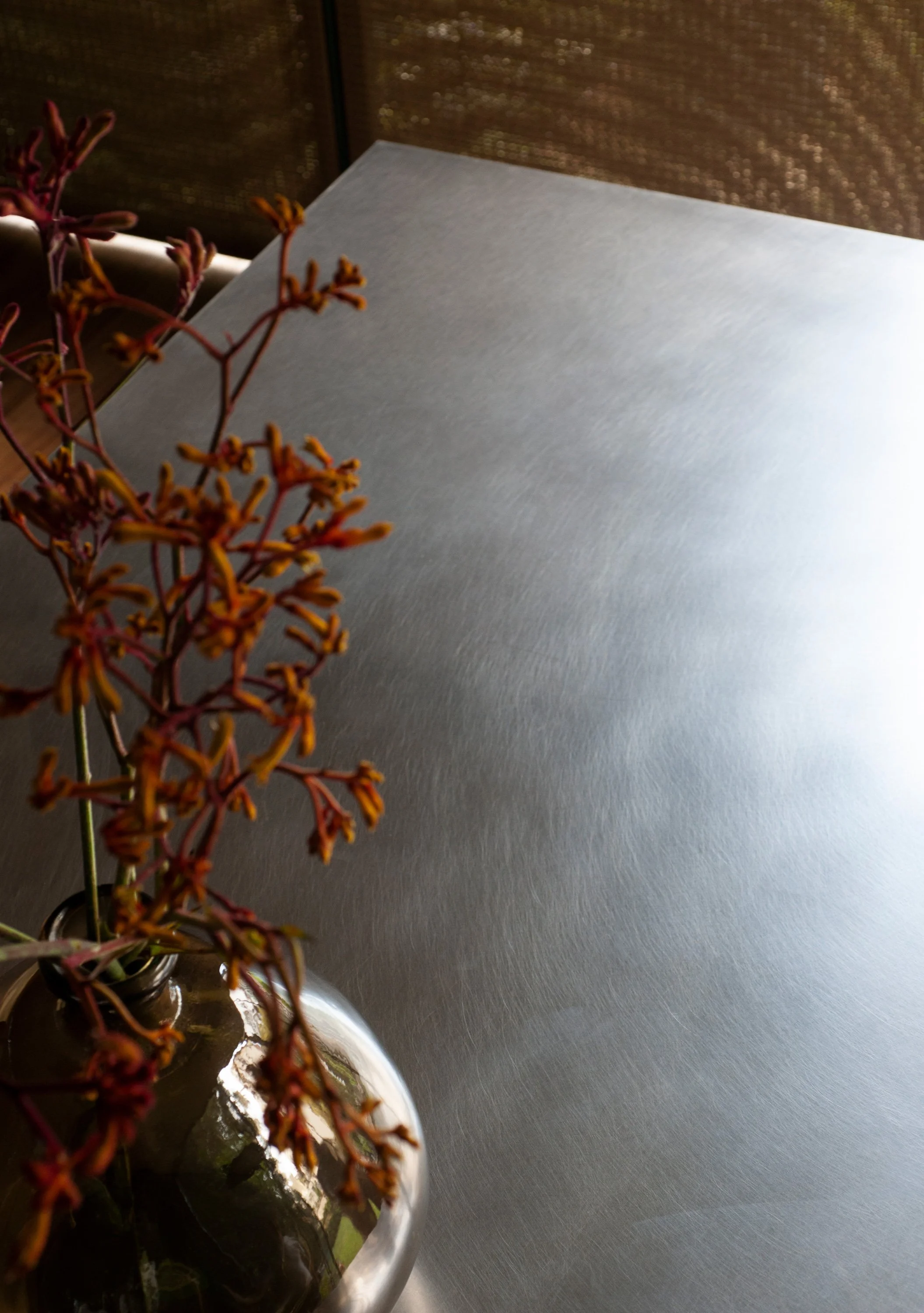 Blumen in einer silbernen Vase auf einem dunklen Tisch, Nahaufnahme vom oberen Teil, Lichtquelle kommt von rechts, Hintergrund ist eine holzvertäfelte Wand.