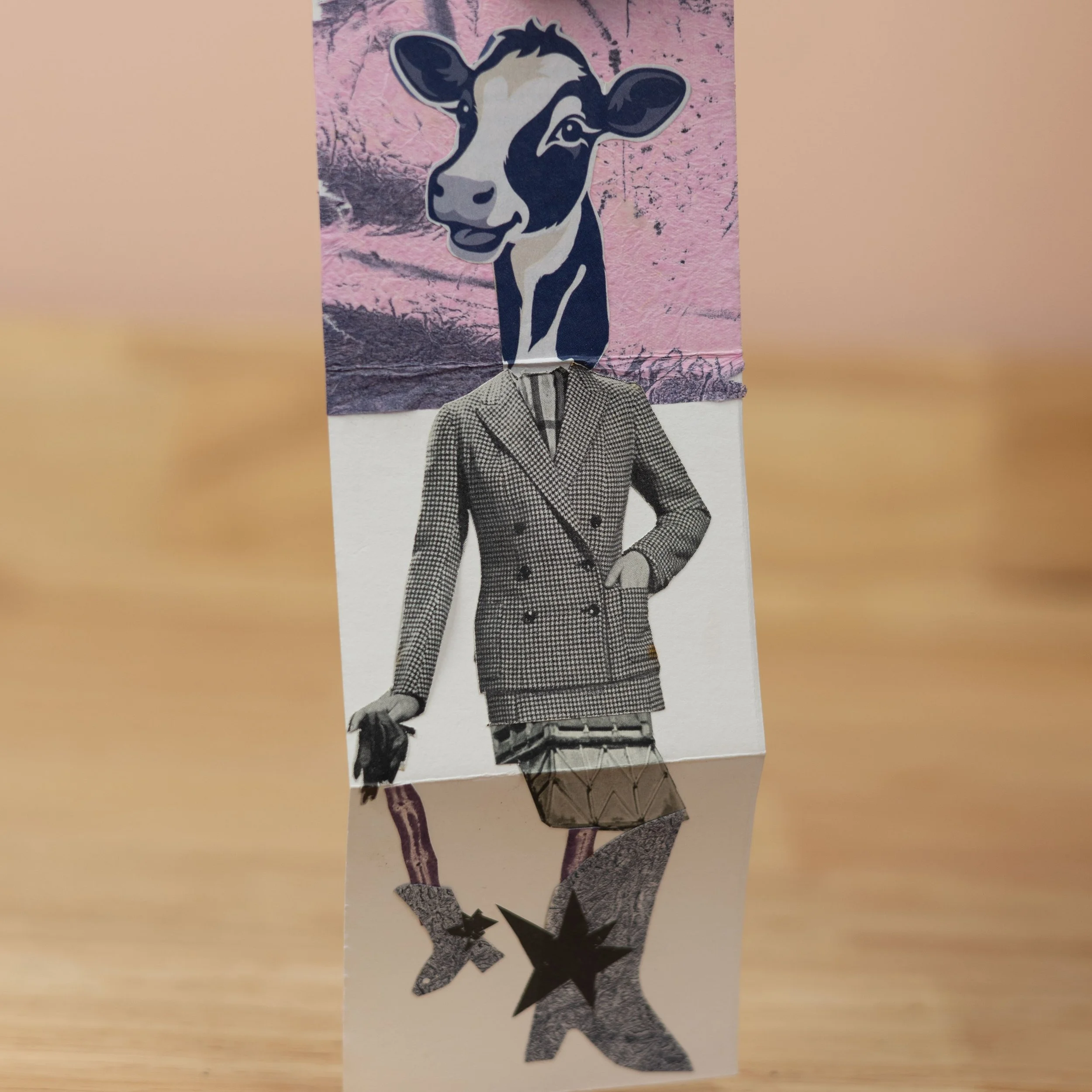 Folded paper zine with a cow's head, houndstooth blazer and mismatched legs, made from collaged and printed elements