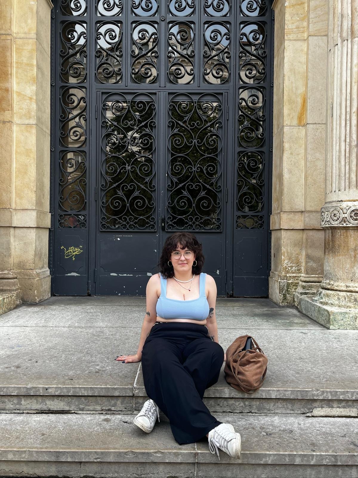 Dominika, founder of Pretty Online Club, sitting on steps in front of an ornate iron gate in France