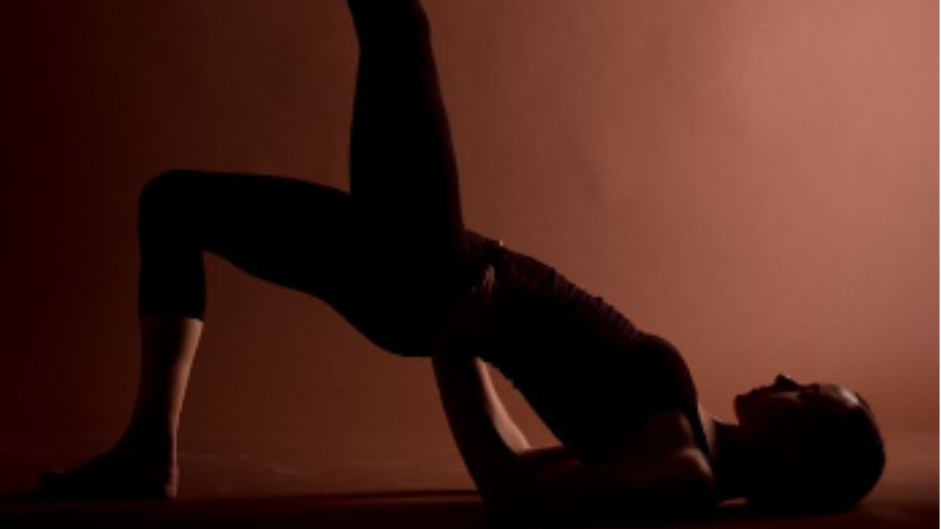A person performing a yoga pose in silhouette against a warm, reddish-brown background.