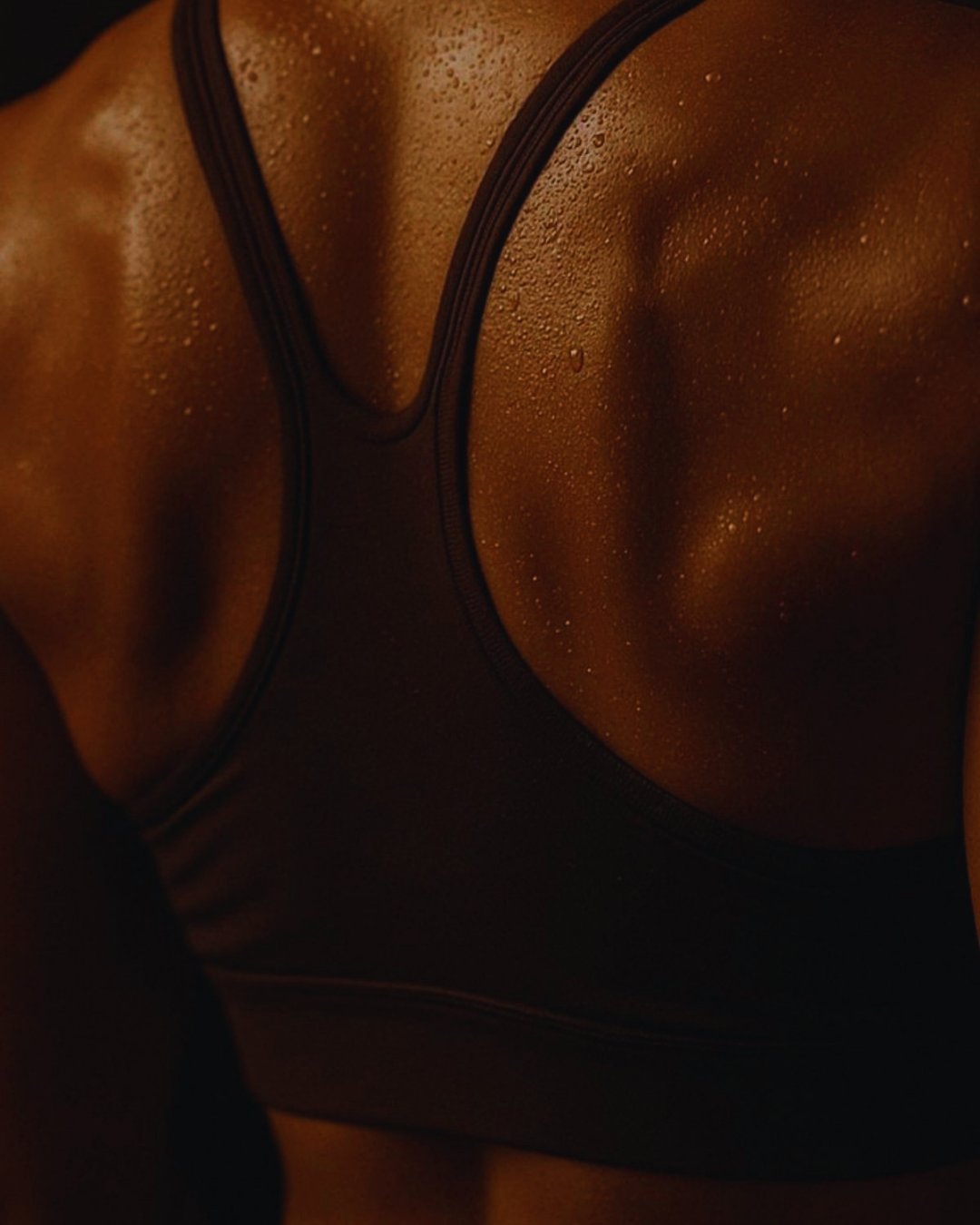 Close-up of a woman's torso in a black, wet, shiny top with water droplets on her skin.