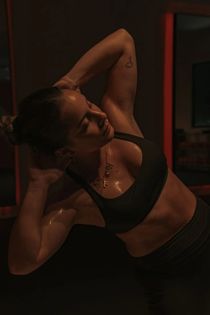 Woman doing a workout, resting with her hands behind her head in a dimly lit gym.