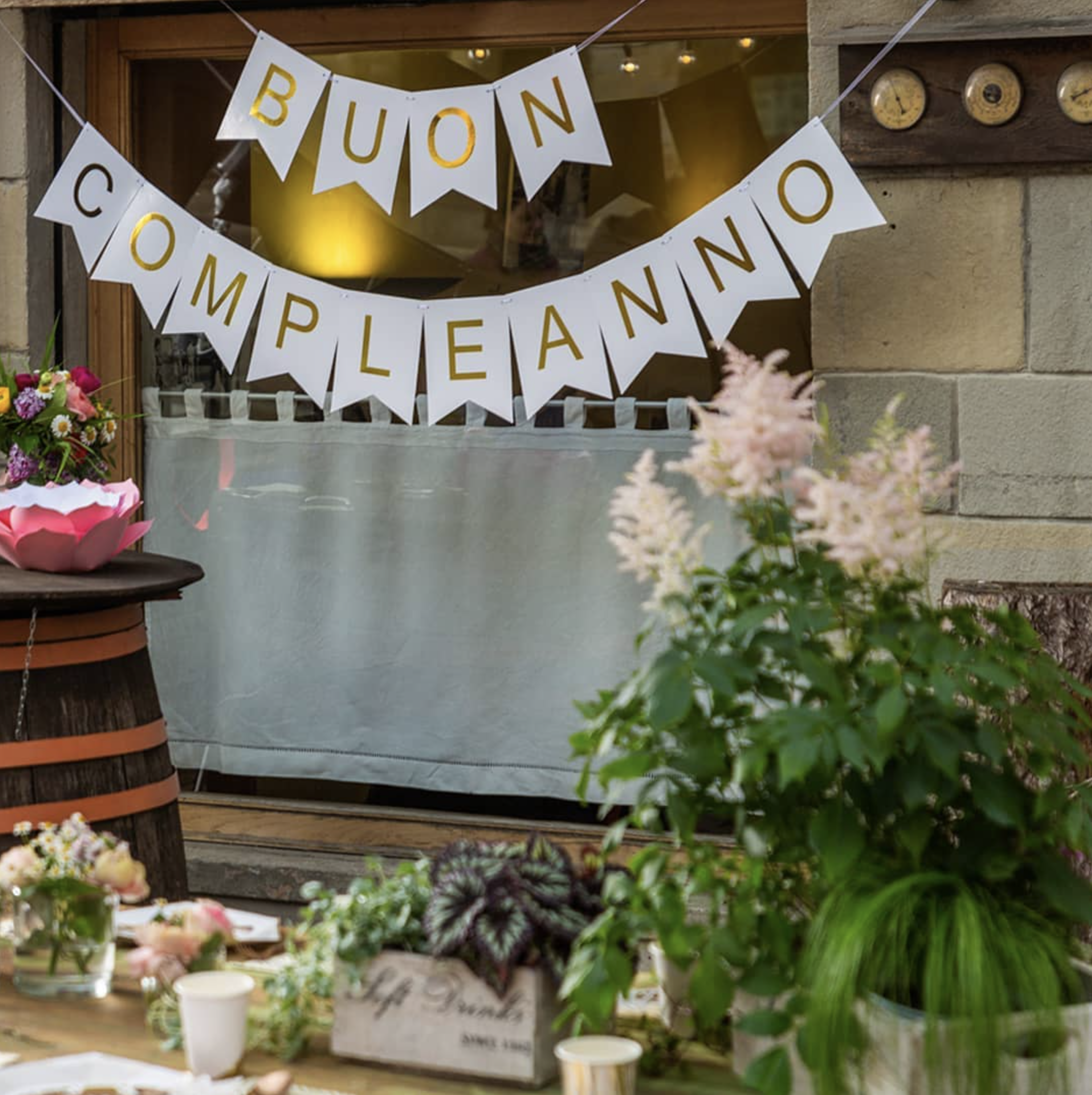 Decorazione con banner bianco e oro che dice 'Buon Compleanno' sul vetro di un negozio o ristorante a Loiano Bologna, con fiori di fronte.