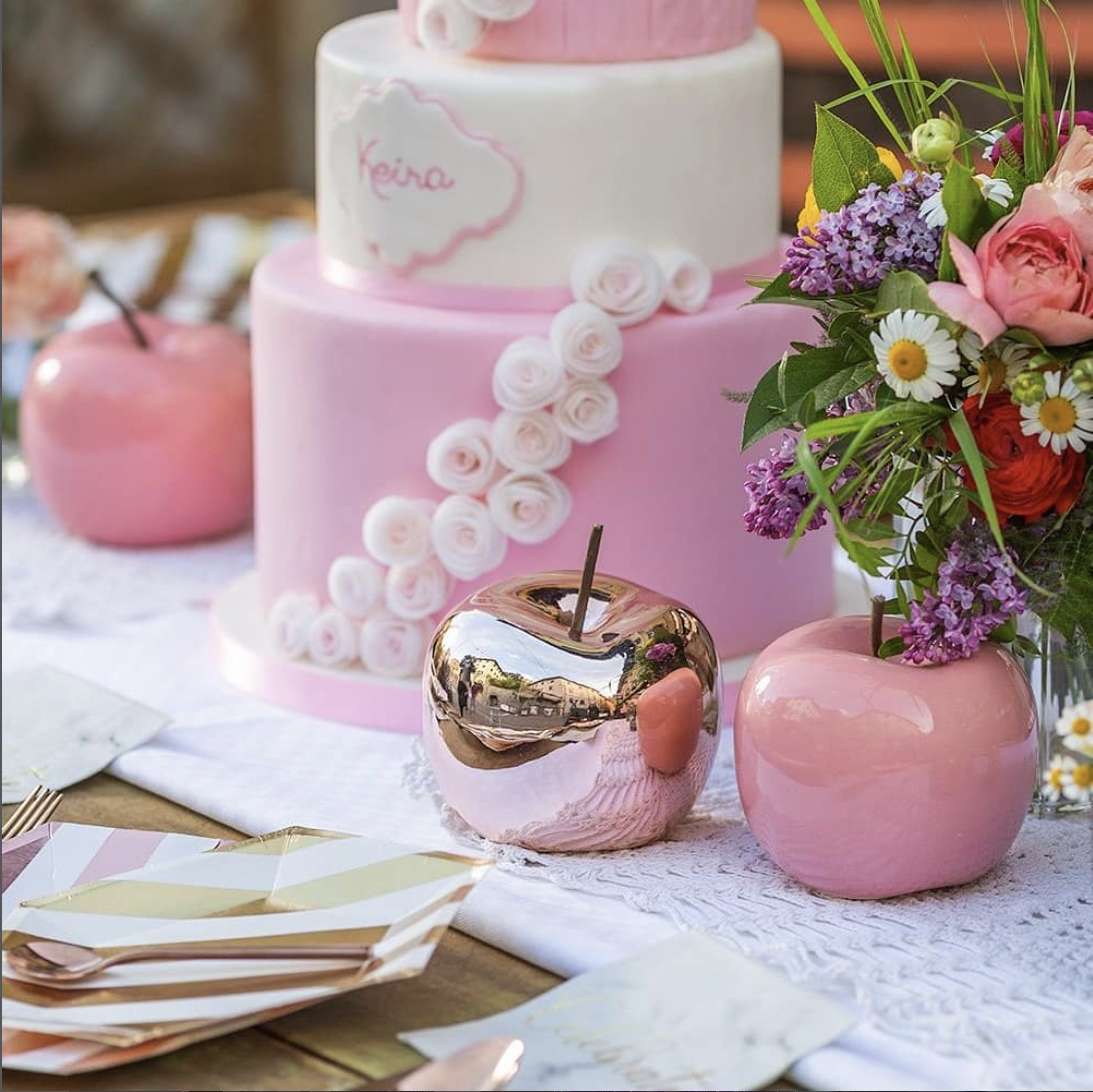 Torta decorata con fiori in pasta di zucchero rosa e un'etichetta con il nome Keira, accompagnata da un bouquet di fiori colorati