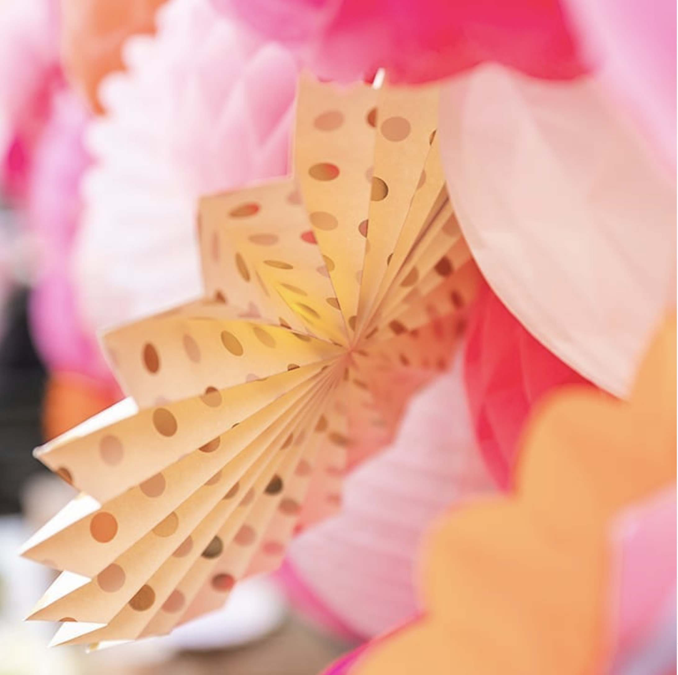 Barattoli di carta colorata con fori, decorati con colori caldi, su un sfondo sfocato con tonalità rosa e arancioni.