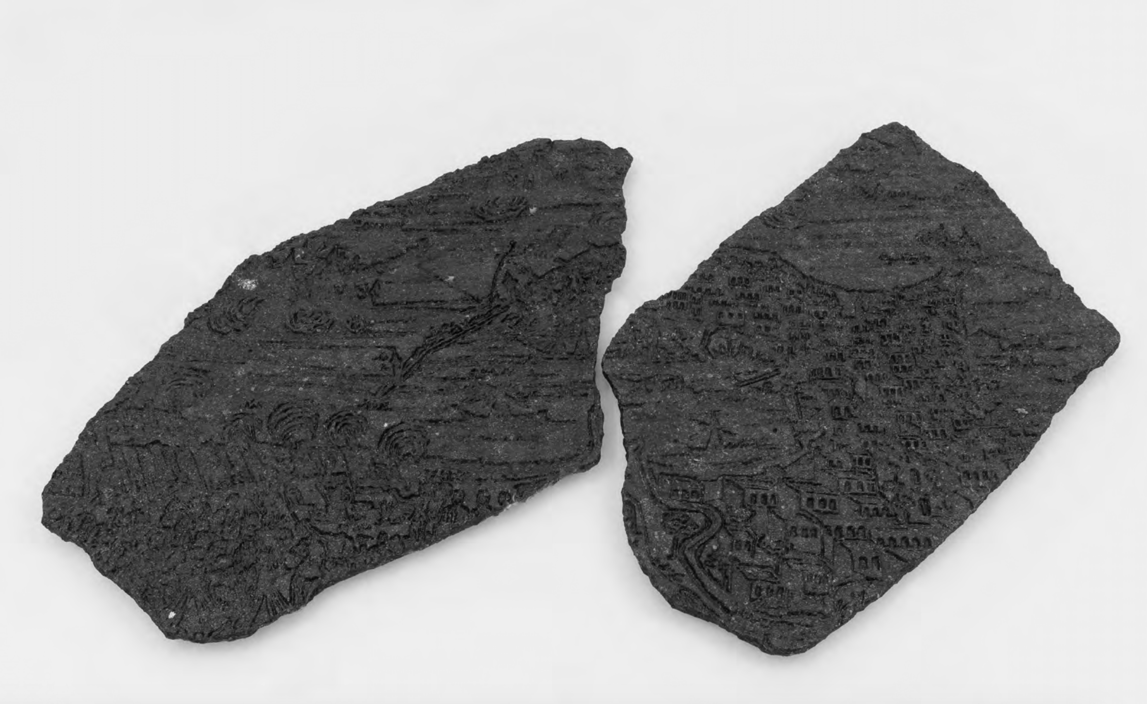 Two black volcanic rocks with intricate carvings and engravings, placed on a white surface.