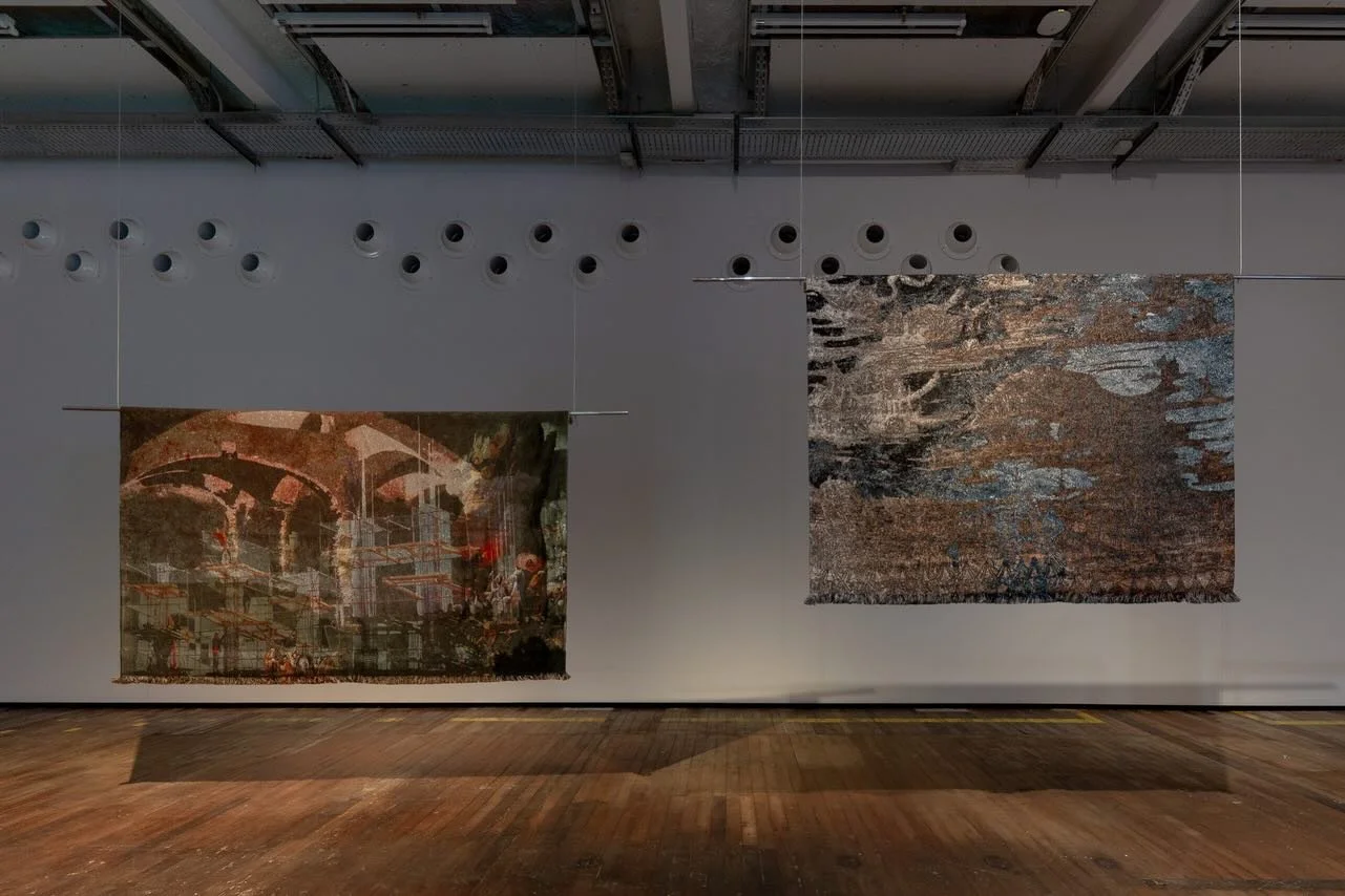 Two textile art pieces hanging in a gallery with white walls and wooden floors.