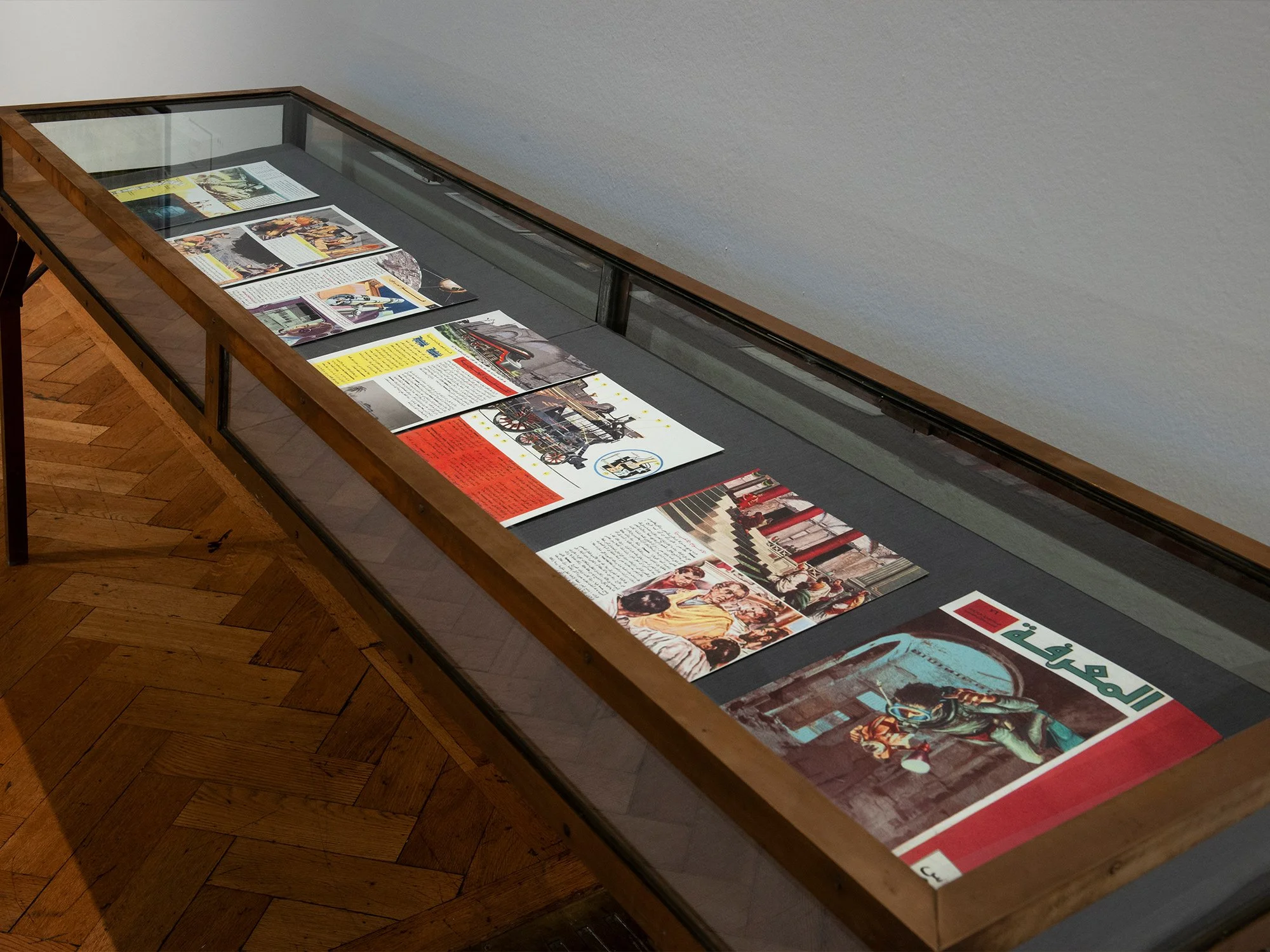 A glass display case showcasing vintage magazines and newspapers laid flat on black fabric inside a wooden framed case.
