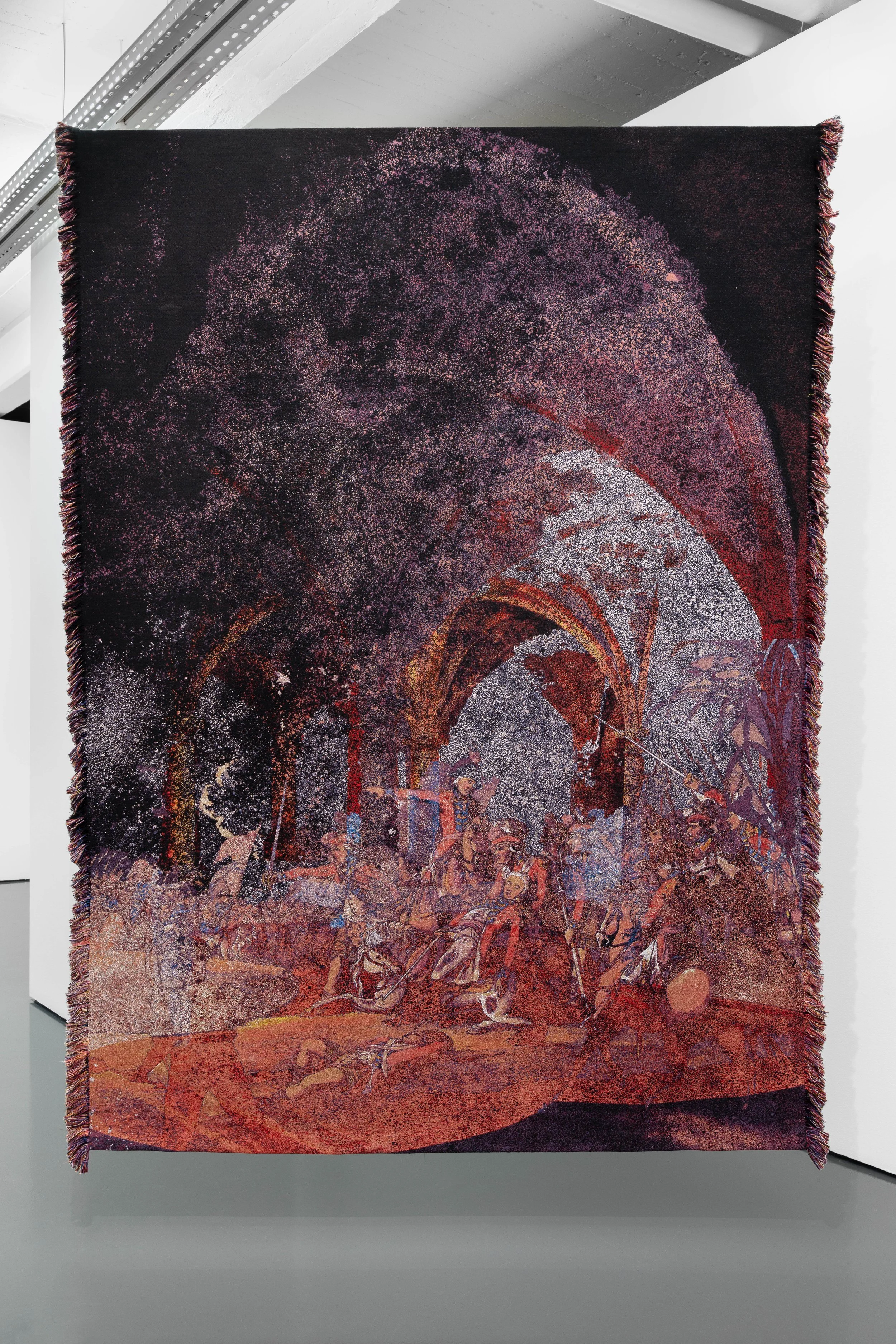 An artwork or tapestry with a predominantly dark background and intricate, colorful stamps or dots, forming a pattern that transitions from darker at the top to reddish at the bottom, displayed on a white gallery wall.