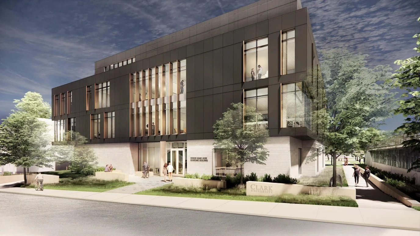 A modern multi-story academic building with dark exterior panels, large windows, and wooden accents, situated on a landscaped campus with trees and walkways.