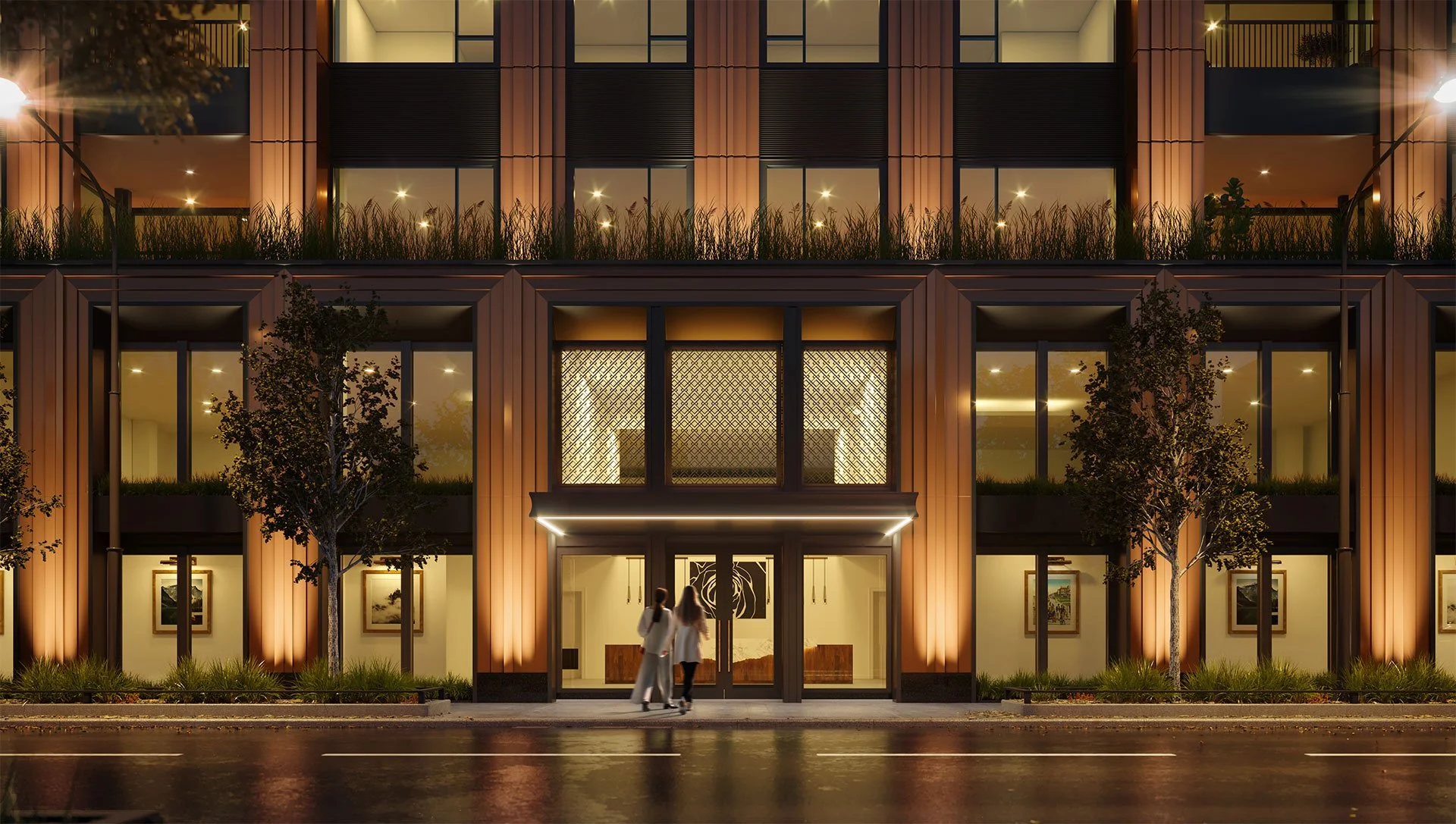 Night view of a modern multi-story building with large glass windows, warm lighting, and outdoor greenery. Two people are walking in front of the entrance.