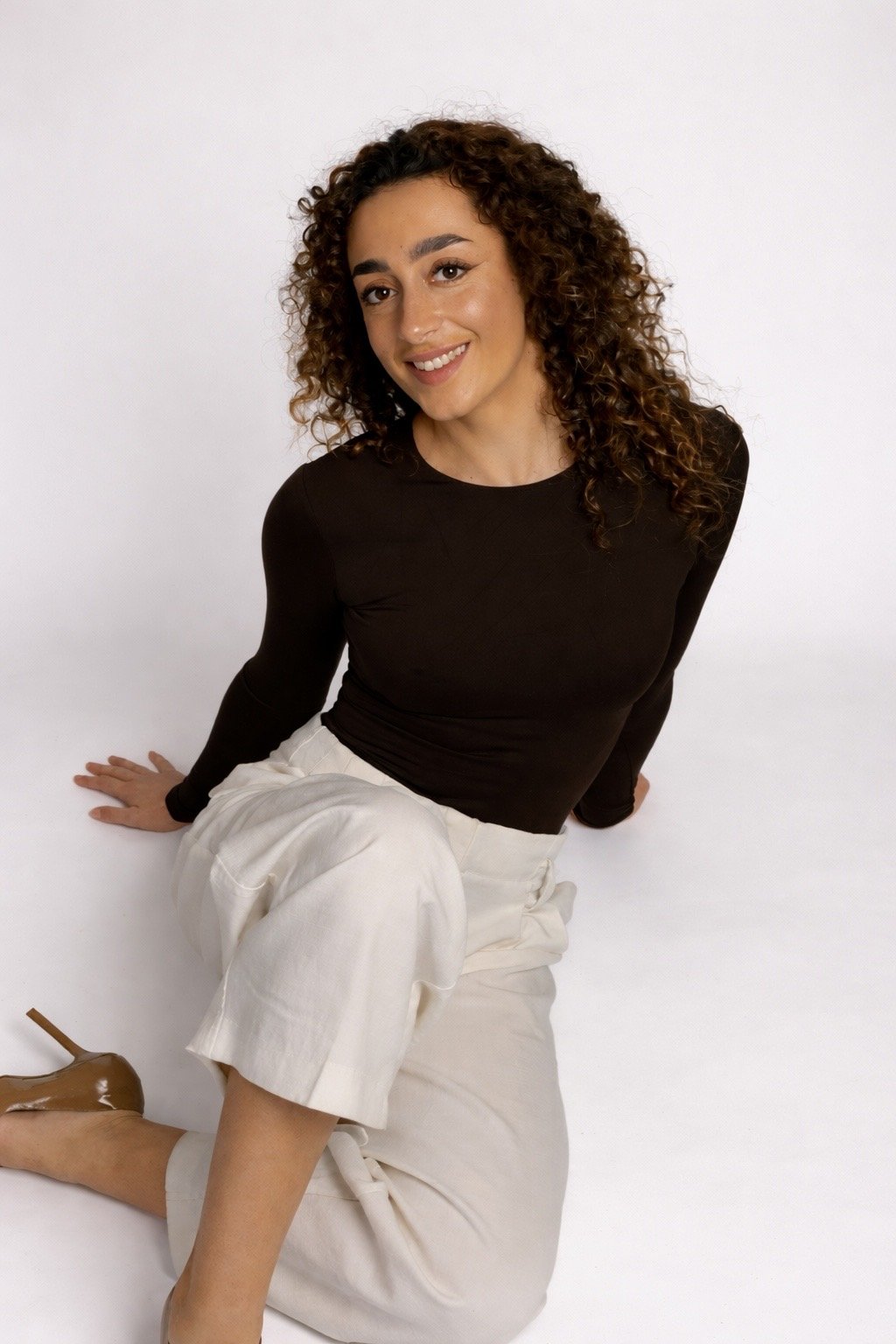Portrait d'une jeune femme aux cheveux bouclés, portant une chemise blanche, sur fond gris.