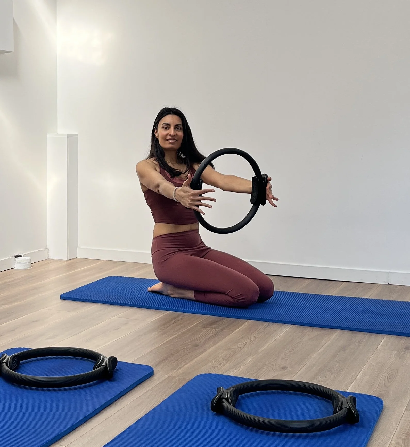 Une femme avec de longs cheveux noirs portant un débardeur blanc, debout dans une pièce avec un fond neutre.