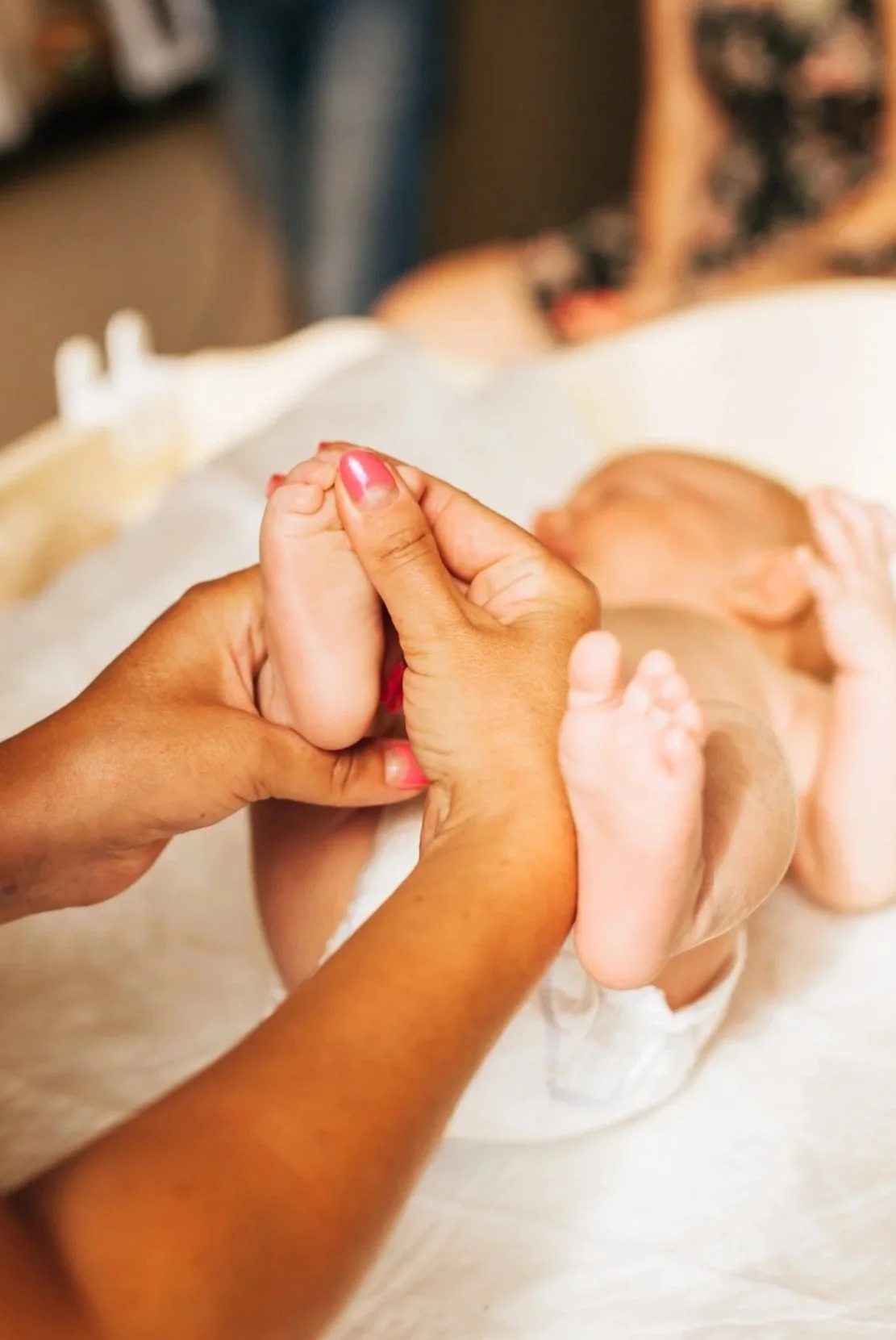 les mains d'une femme entrain de masser les pieds de son bébé dans un cadre chaleureux en Essonne