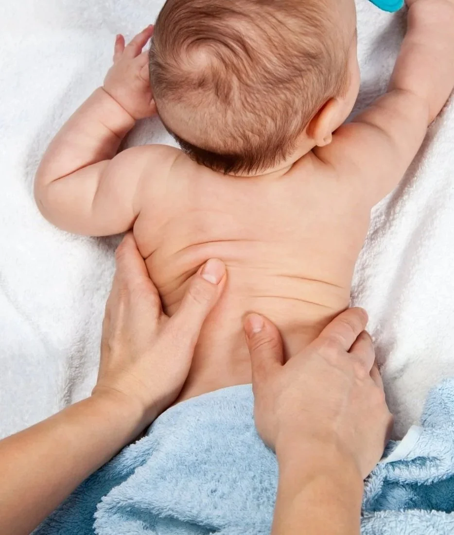 Un bébé allongé sur le ventre, vu de derrière, avec un adulte qui lui donne un massage du dos.