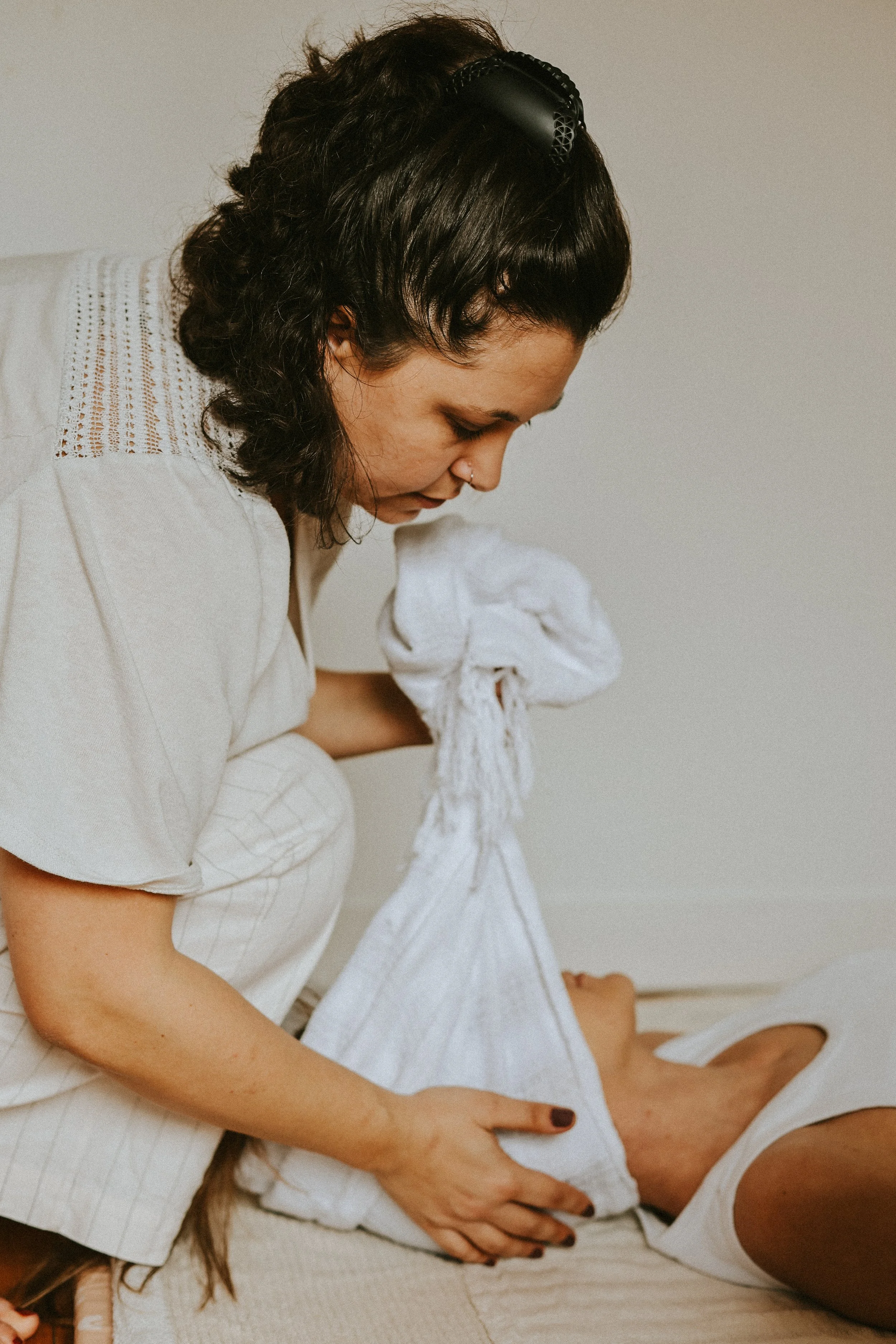 Une femme avec des cheveux bruns foncés entrain de faire un soin rebozo sur la tête d'une autre femme