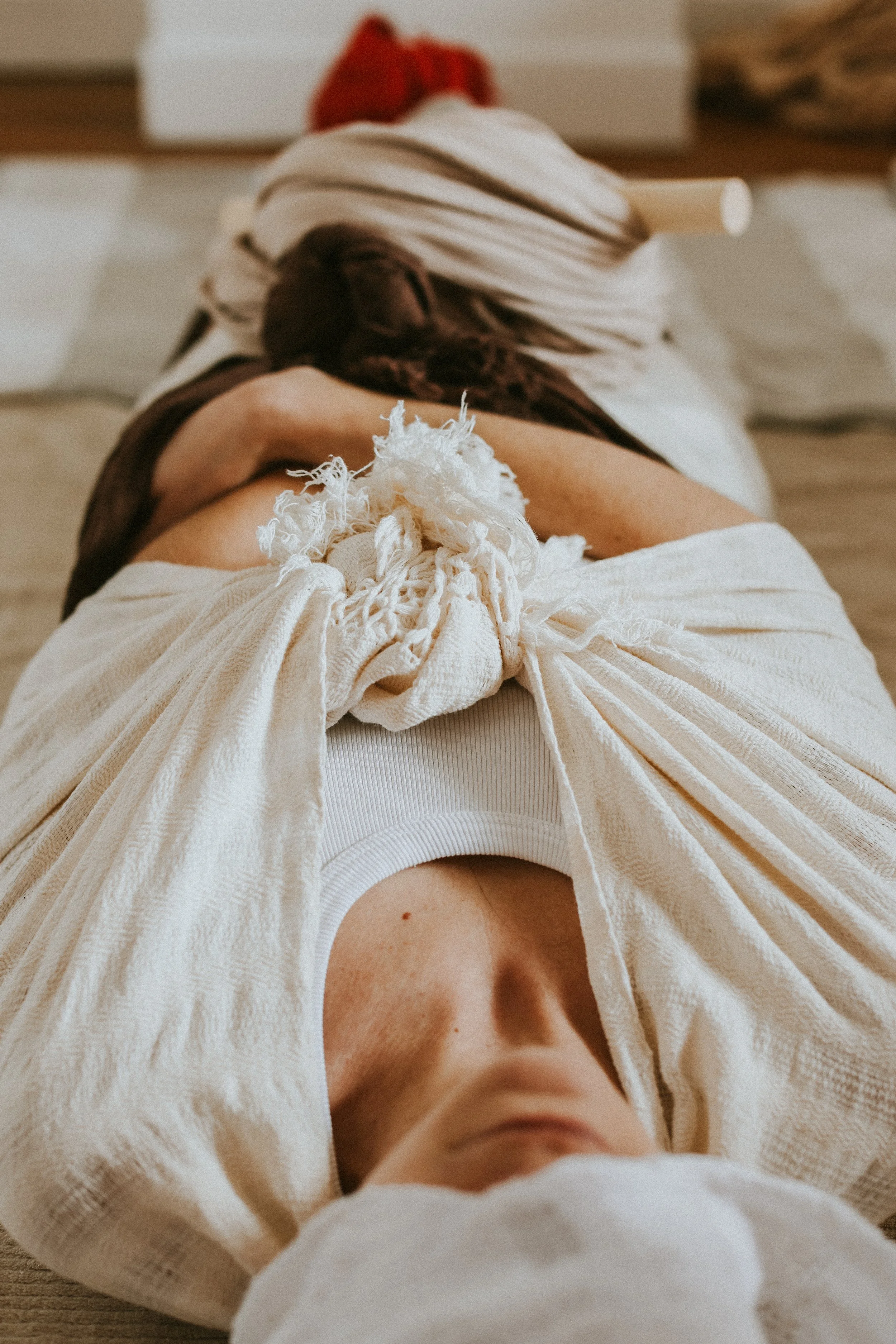 Vue en plongée d'une personne allongée, avec 7 rebozo entrain de lui resserrer tout le corps lors d'un soin rebozo post-partum.
