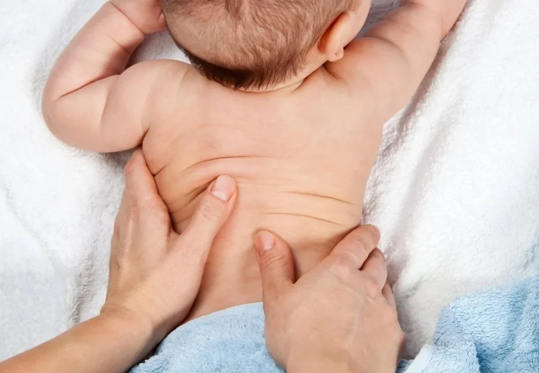 les mains d'une maman entrain de masser le dos de son bébé tout potelé dans une ambiance calme et sereine.