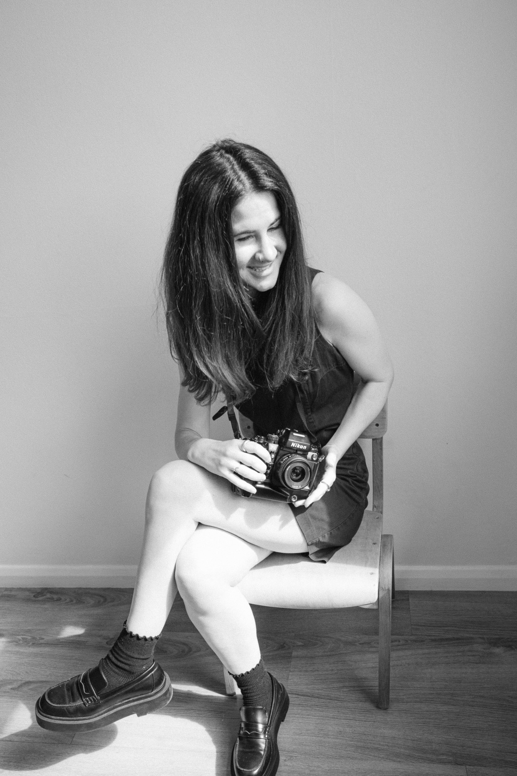 Black and white portrait of London wedding photographer Nadine Faria holding her camera