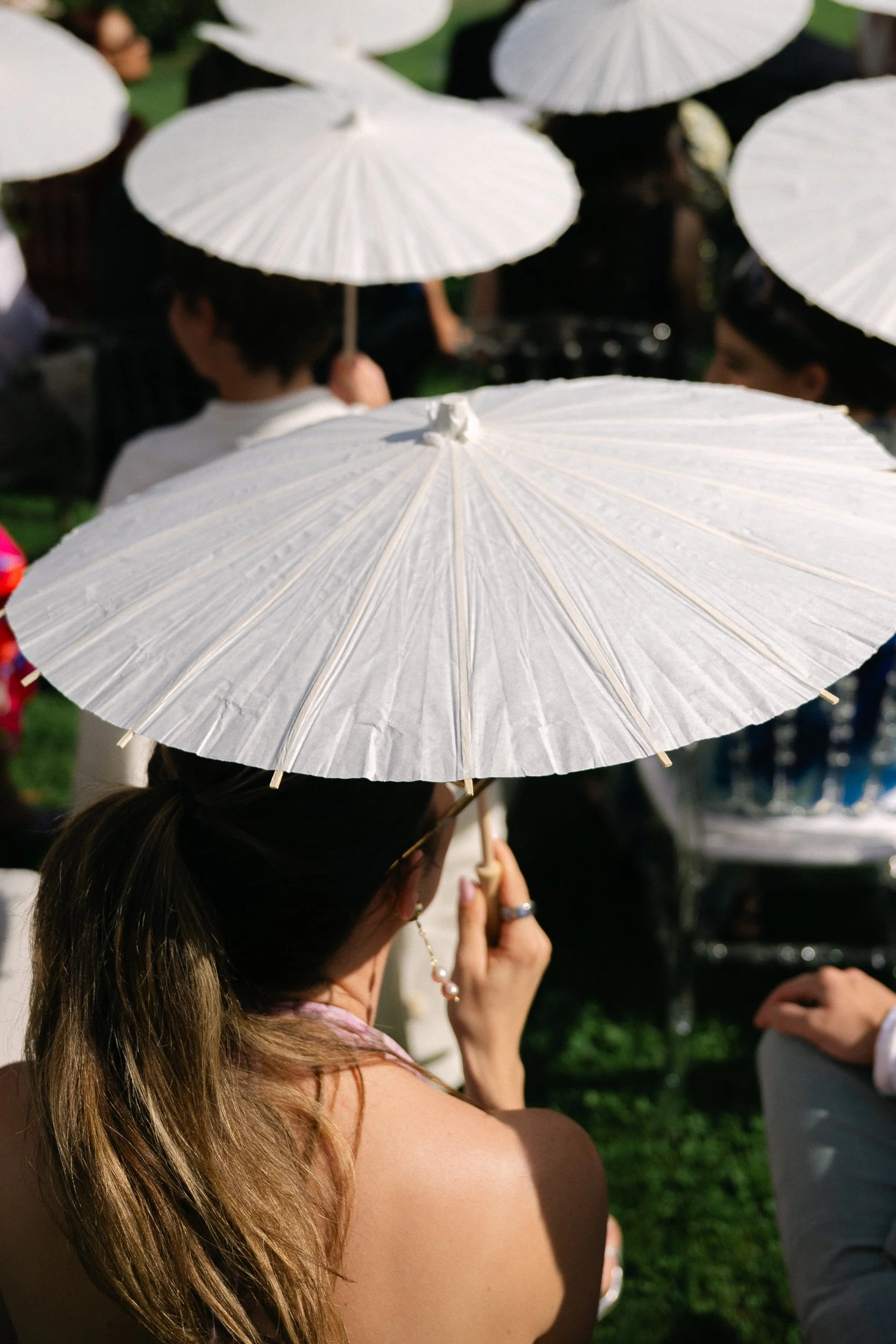 Guests sheltering under white parasols during an outdoor ceremony at Château Fengari