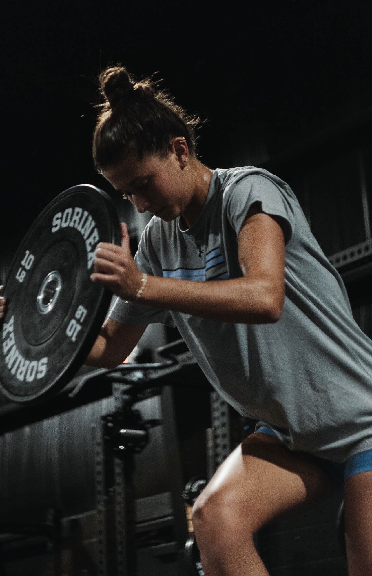 A woman putting a weighted plate on gym equipment