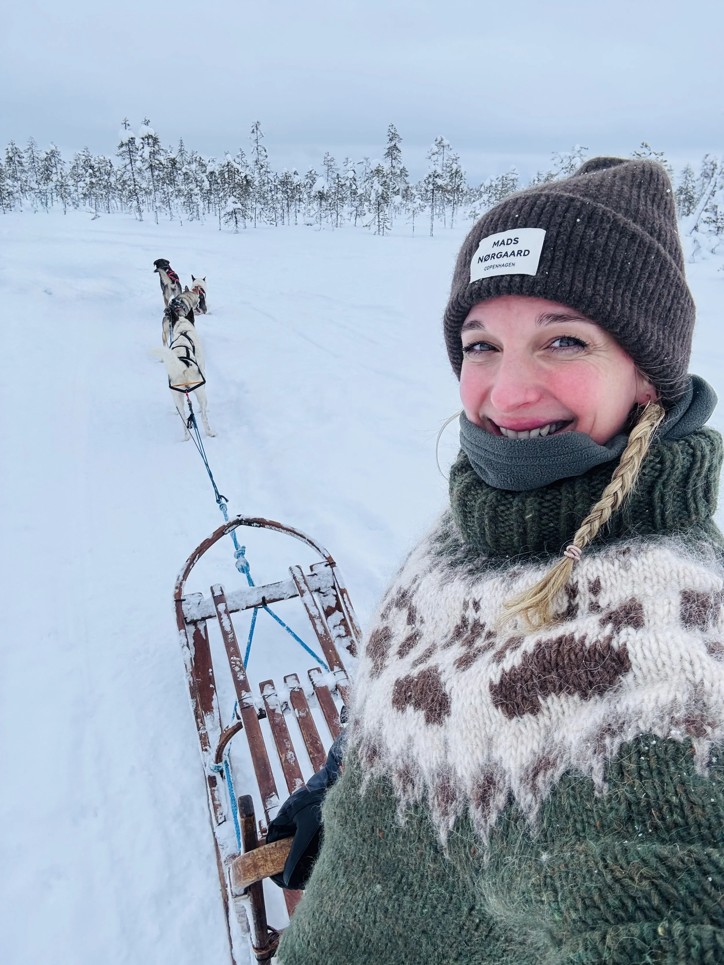 Eine Frau in Winterkleidung, die auf einem Schlitten in verschneitem Winterwald mit Schnee bedeckten Bäumen sitzt, während sie sich fotografiert.
