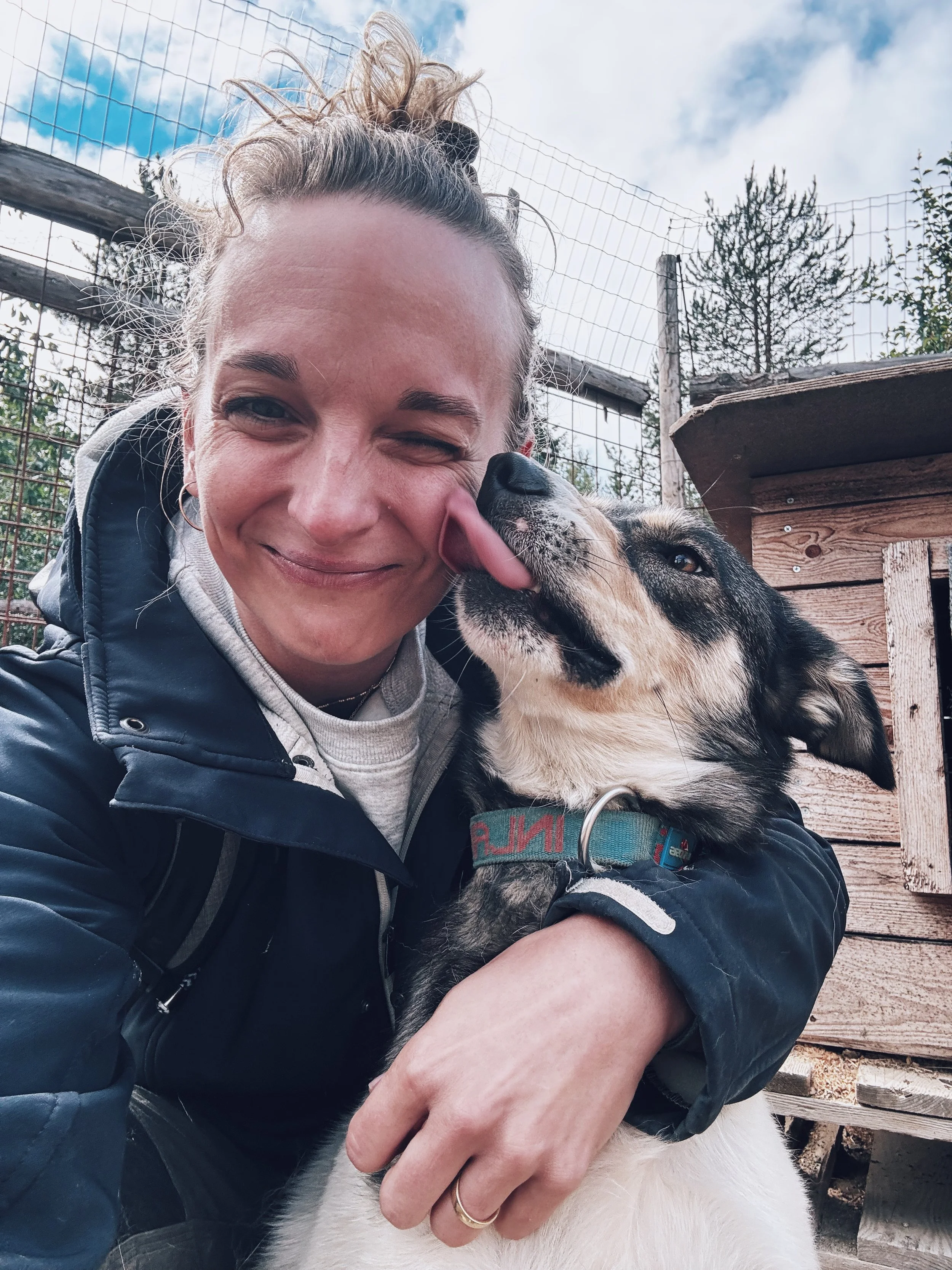 Eine Frau mit einem Hund, die im Freien auf einer Holzstruktur sitzt, während sie den Hund streichelt.