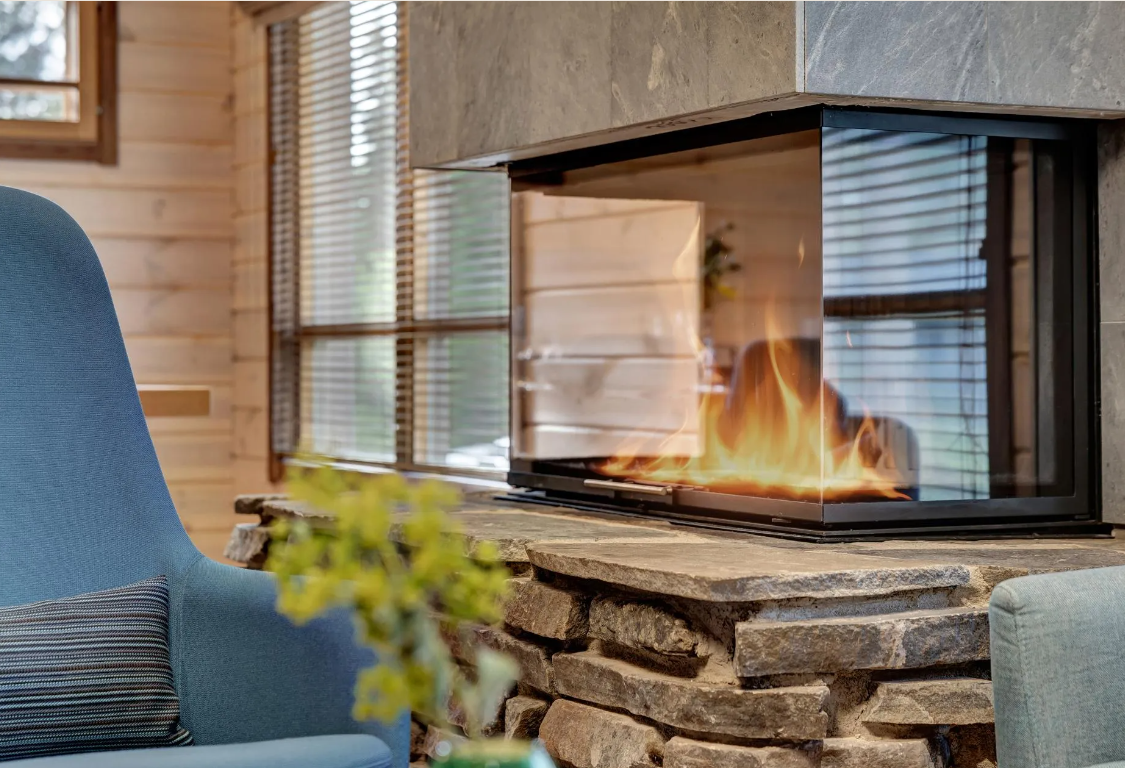 Blick auf einen modernen Kamin mit Glasfront, der Flammen zeigt, in einem gemütlichen Wohnzimmer mit Holzverkleidung und großen Fenstern.