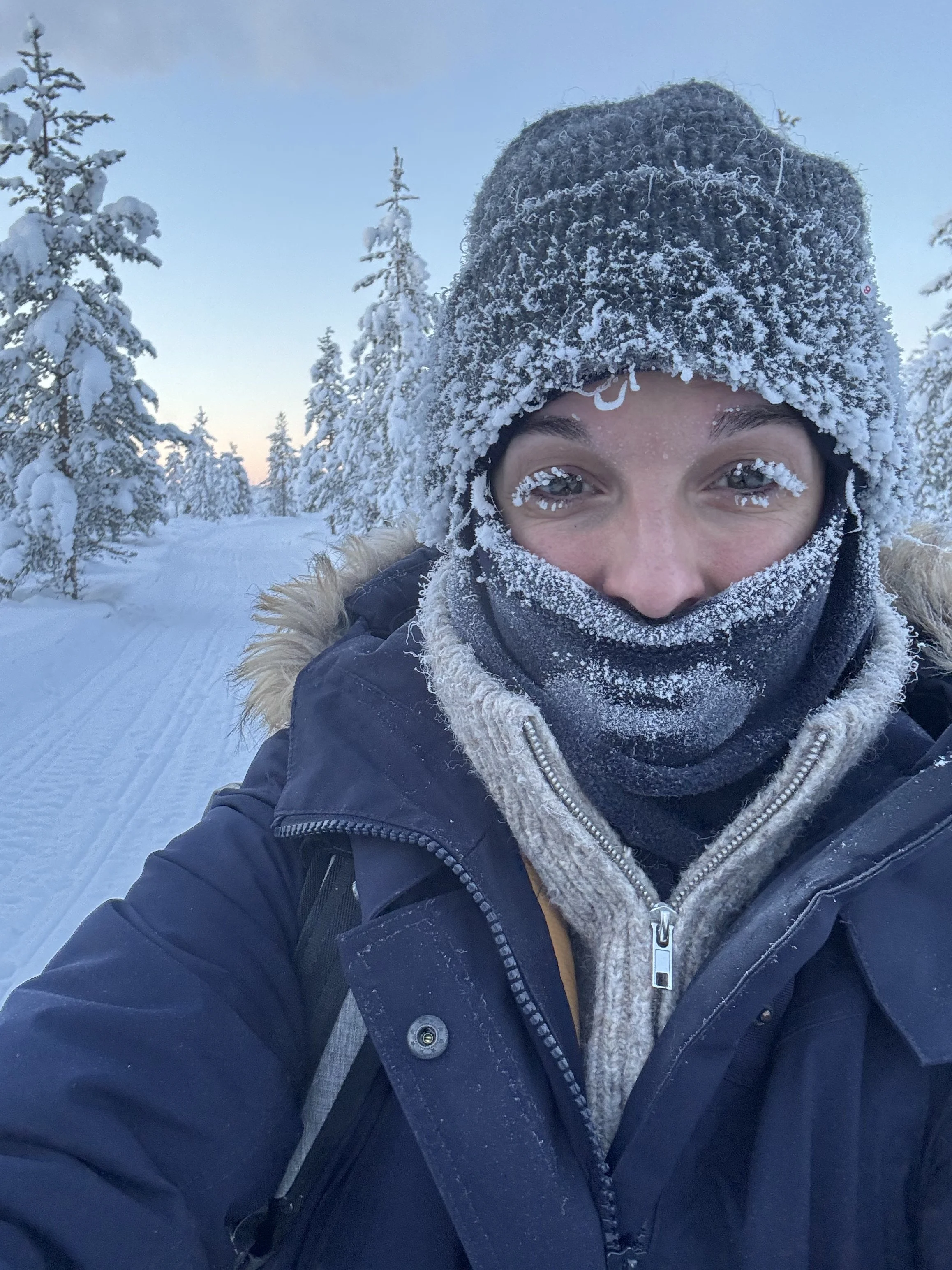 Person in Winterkleidung und Mütze, umgeben von verschneiten Bäumen in einer Schneelandschaft.