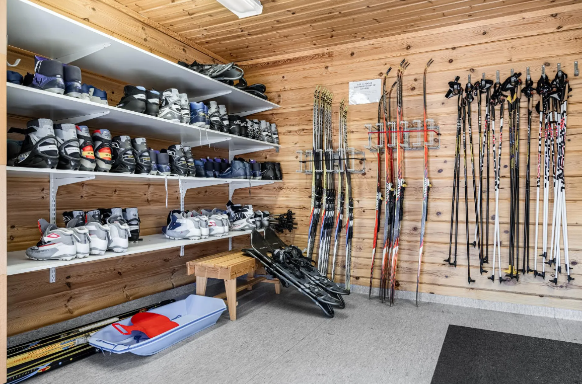 Skiausrüstung in einem Schneesportraum, mit Skischuhen, Skiern und Skistöcken auf Regalen und Wandhaken.