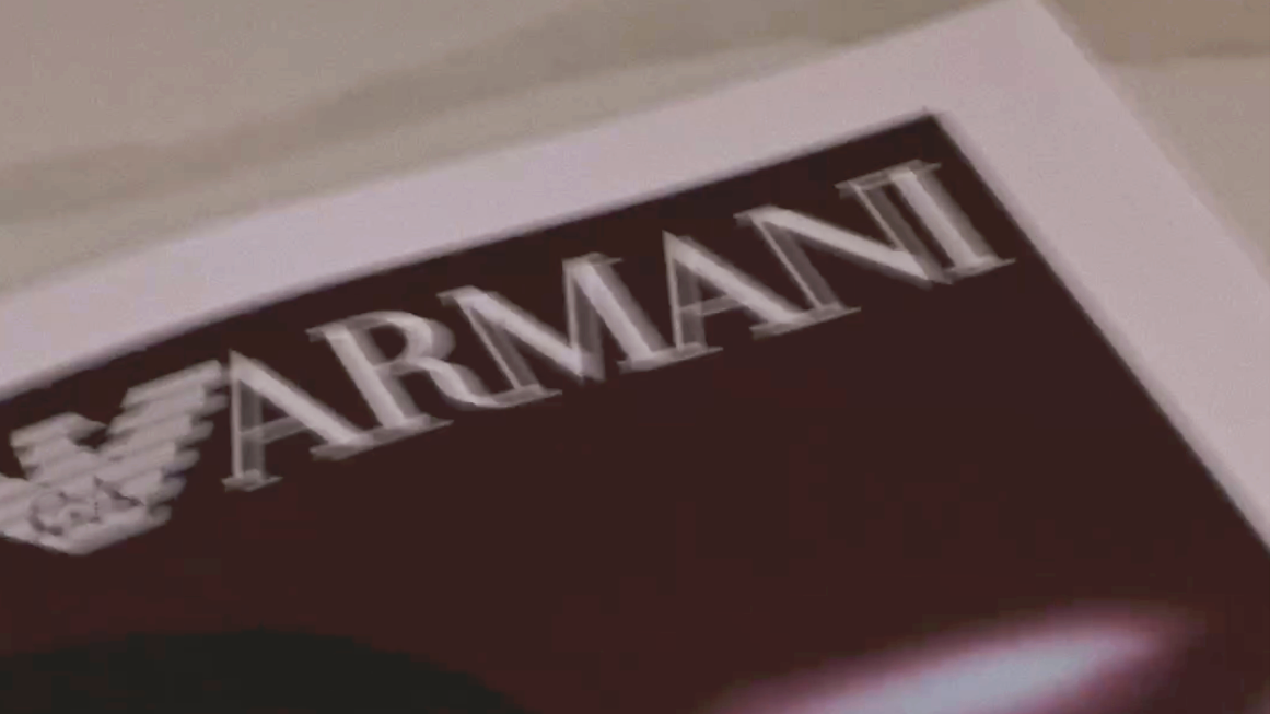Close-up of a branded newspaper with the word 'ARMANI' in white uppercase letters on a dark pink background.
