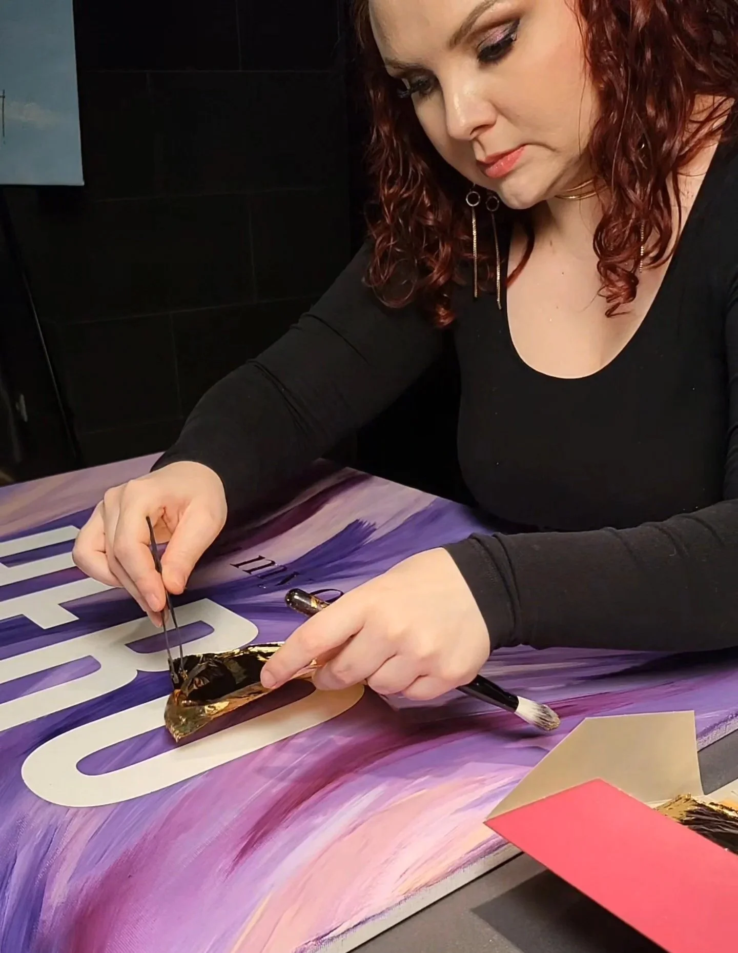 Eine Frau arbeitet an einem bunten Poster und verwendet einen Pinsel mit Goldfarbe.