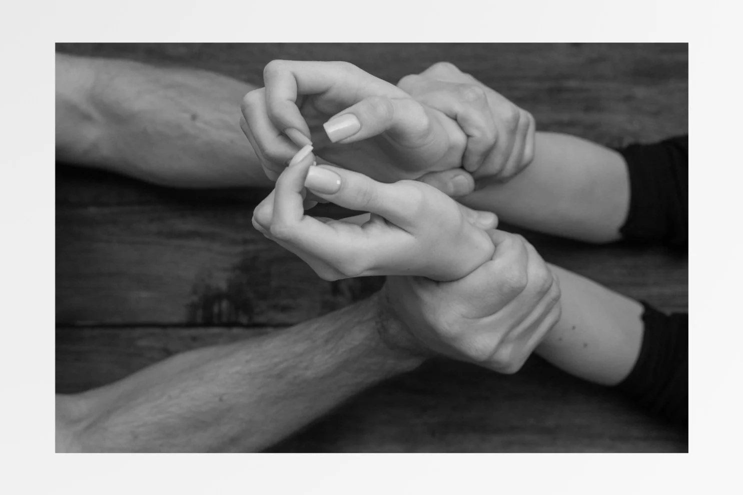 Two pairs of hands demonstrate a first aid technique to stop bleeding, with one hand wrapping a bandage around a person's arm.