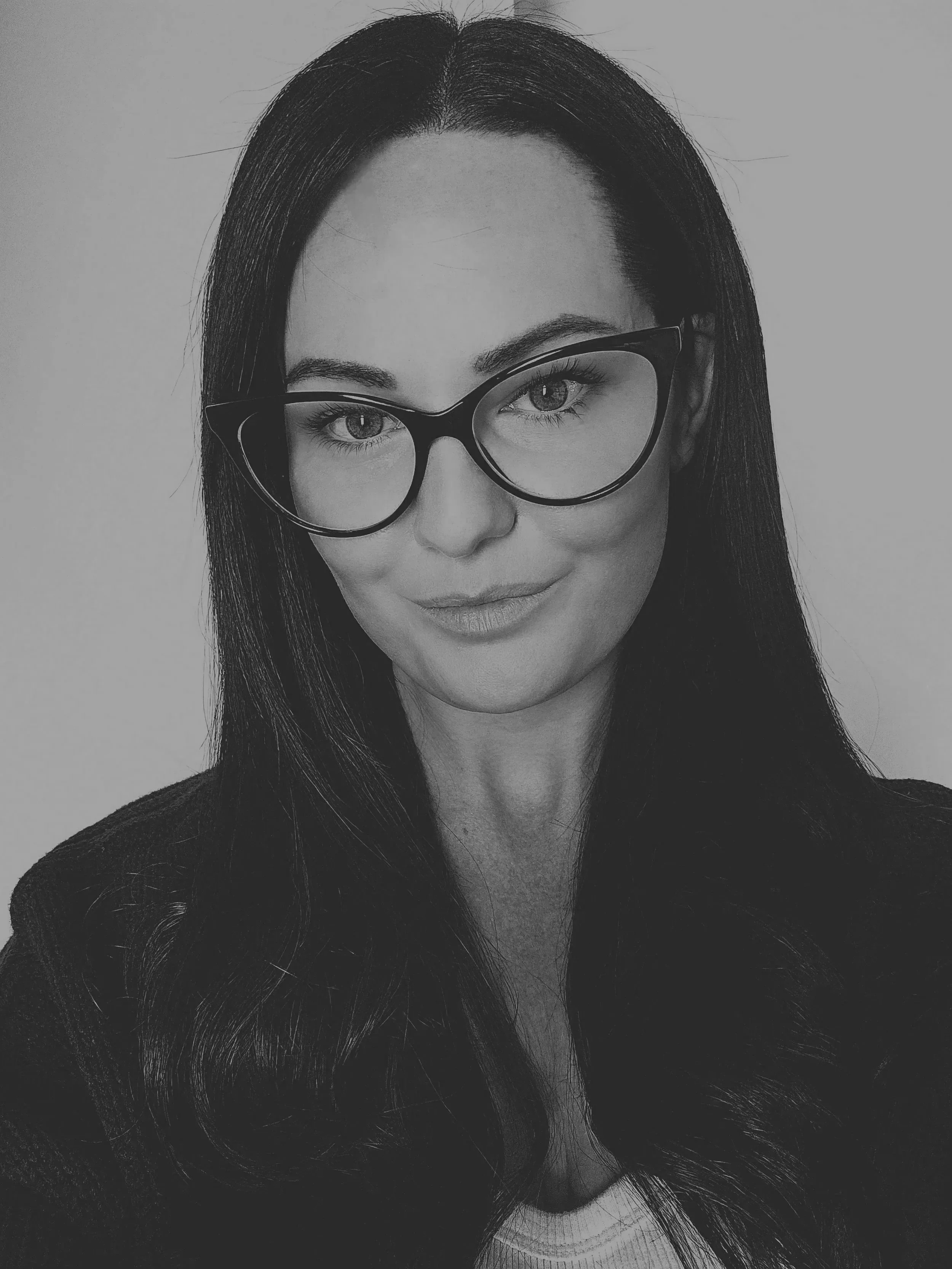 Close-up black and white portrait of a woman wearing glasses, with long straight hair and light makeup, gazing confidently.