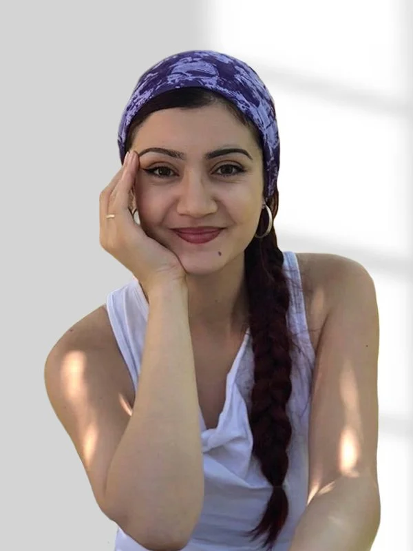 Gülümseyen kadın, mor desenli başlık takmış, beyaz gömlek ve küpe takmış, kırmızı saçlı, uzun örgülü saçlı.