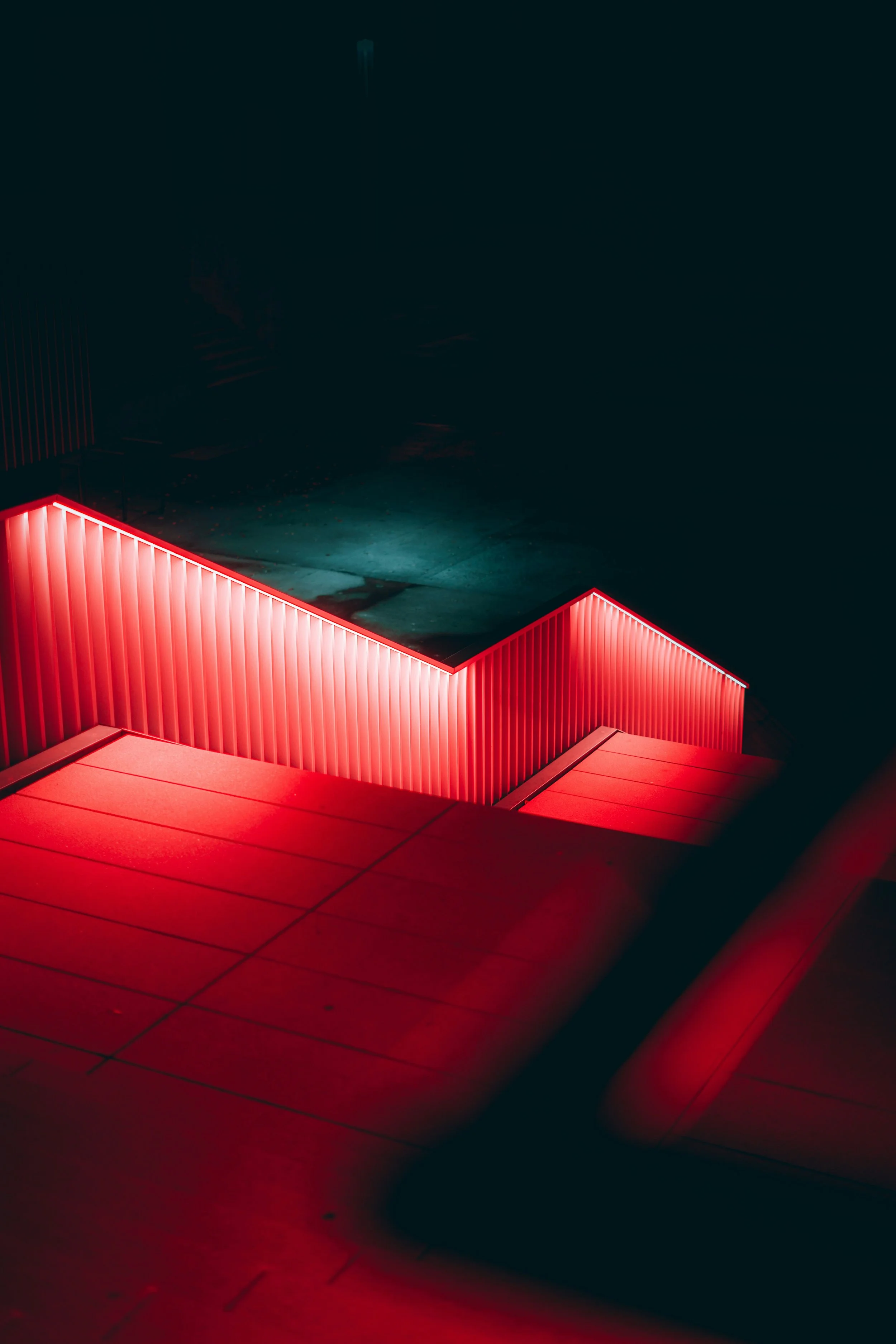 Nighttime view of a staircase with red neon lighting along the railing, leading to a neoclassical building with large columns, illuminated against a dark sky.