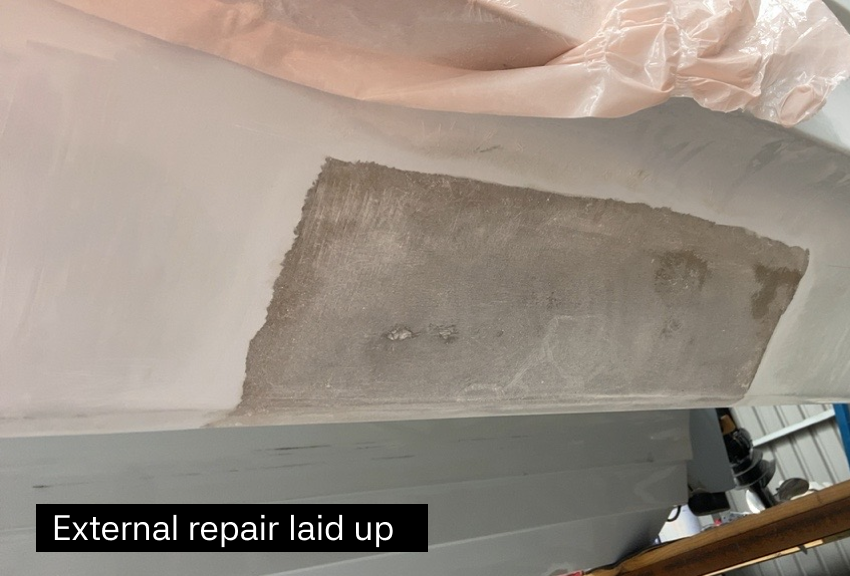 Close-up of a wall showing an area under repair, with patched and sanded drywall in an interior space, and a patch of primer or joint compound. The photo is taken indoors, with tools and materials partially visible in the background.
