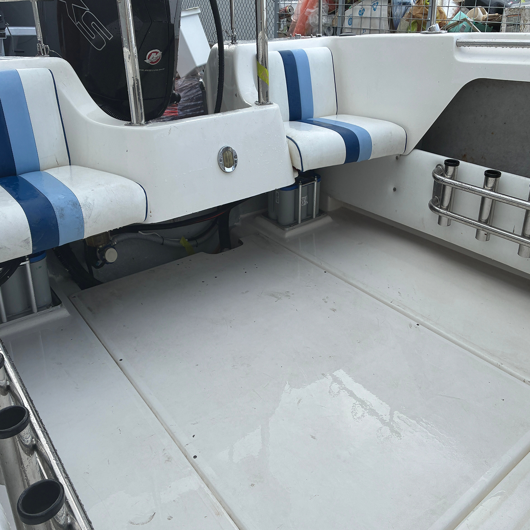 Interior of a white boat with blue striped seats and metal rod holders, some mechanical parts and a black engine visible.