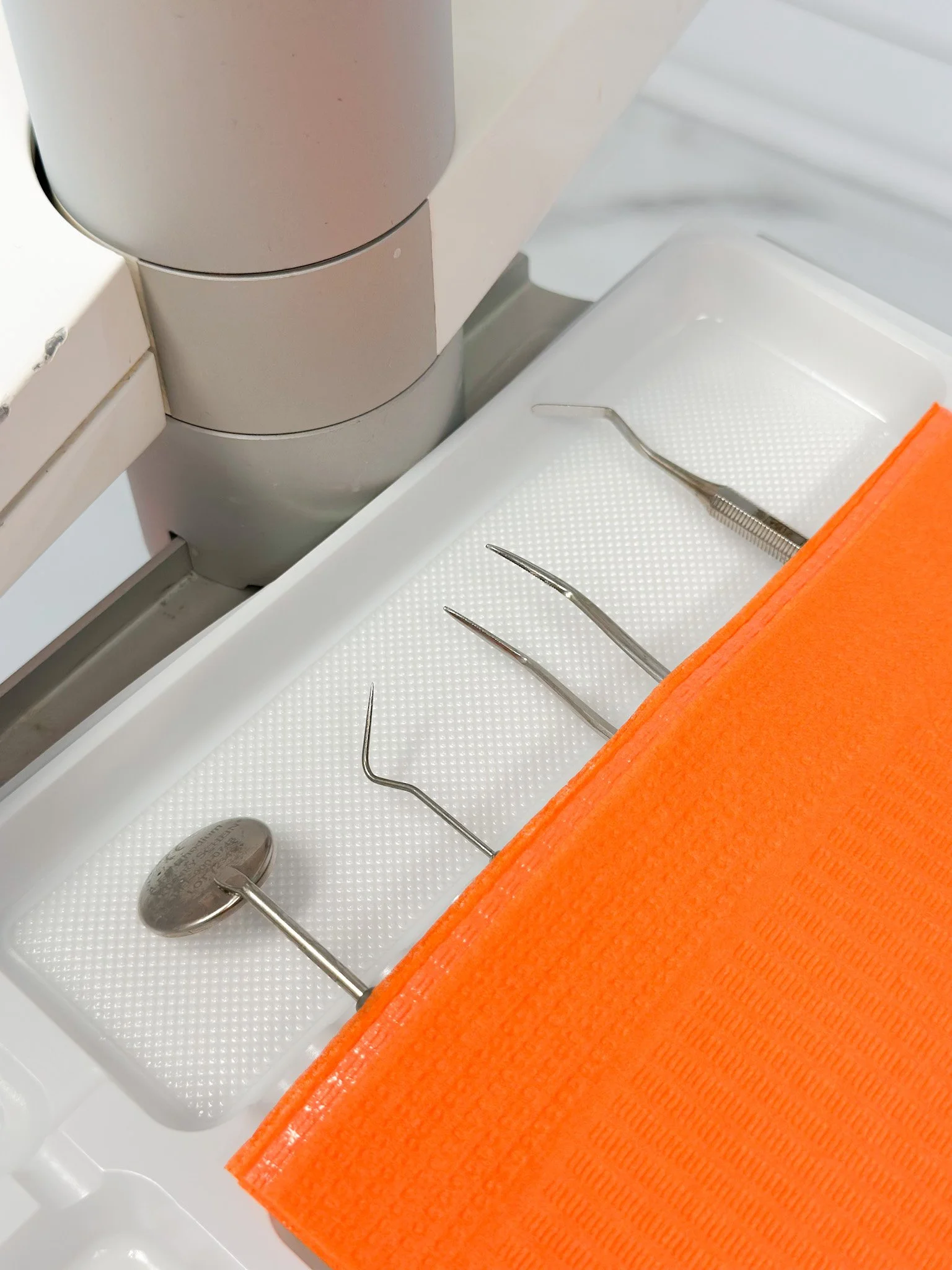 Photo de matériel médical ou d'instruments chirurgicaux, notamment des pinces et un tampon orange, placés dans un tiroir ou une surface blanche.